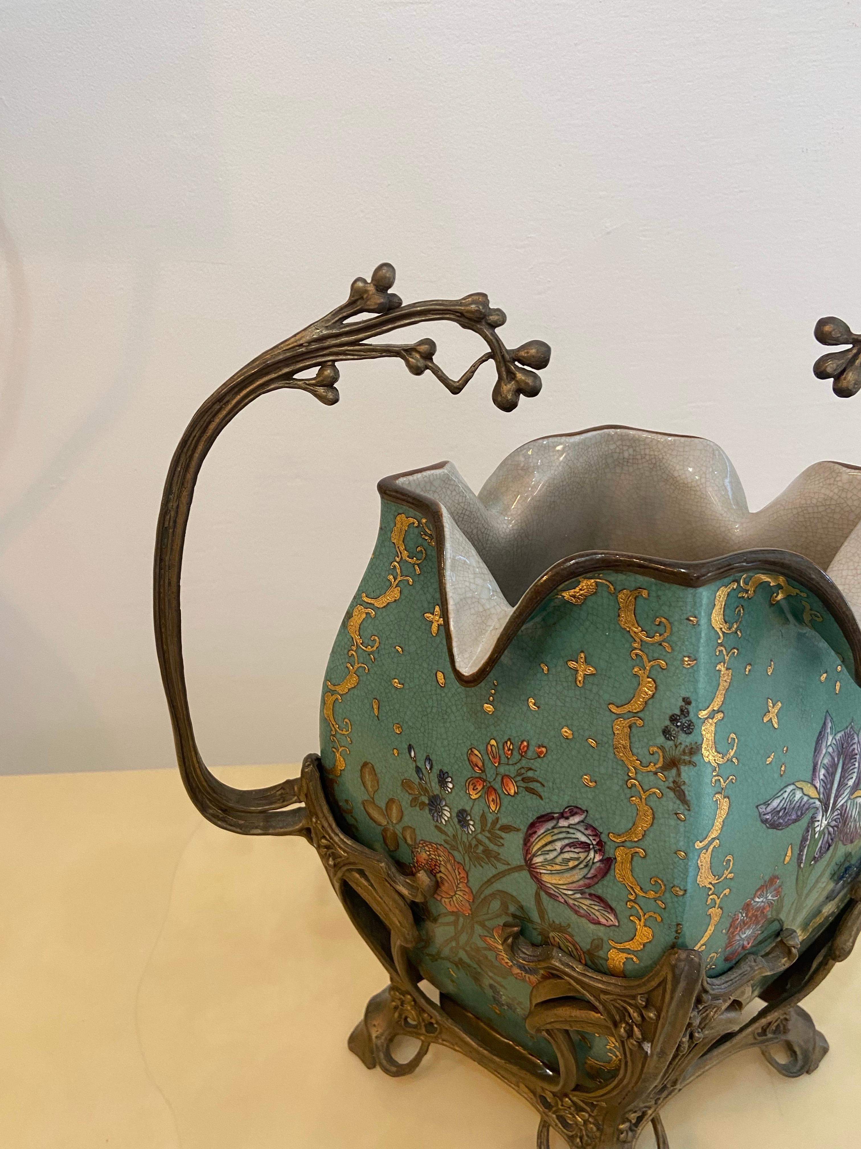 Uno splendido vaso Art Nouveau con intricati motivi floreali dipinti su uno sfondo verde acqua. Il vaso è ornato da accenti dorati ed è sostenuto da manici e base in bronzo ornati, tipici dello stile Art Nouveau. La lavorazione evidenzia le linee