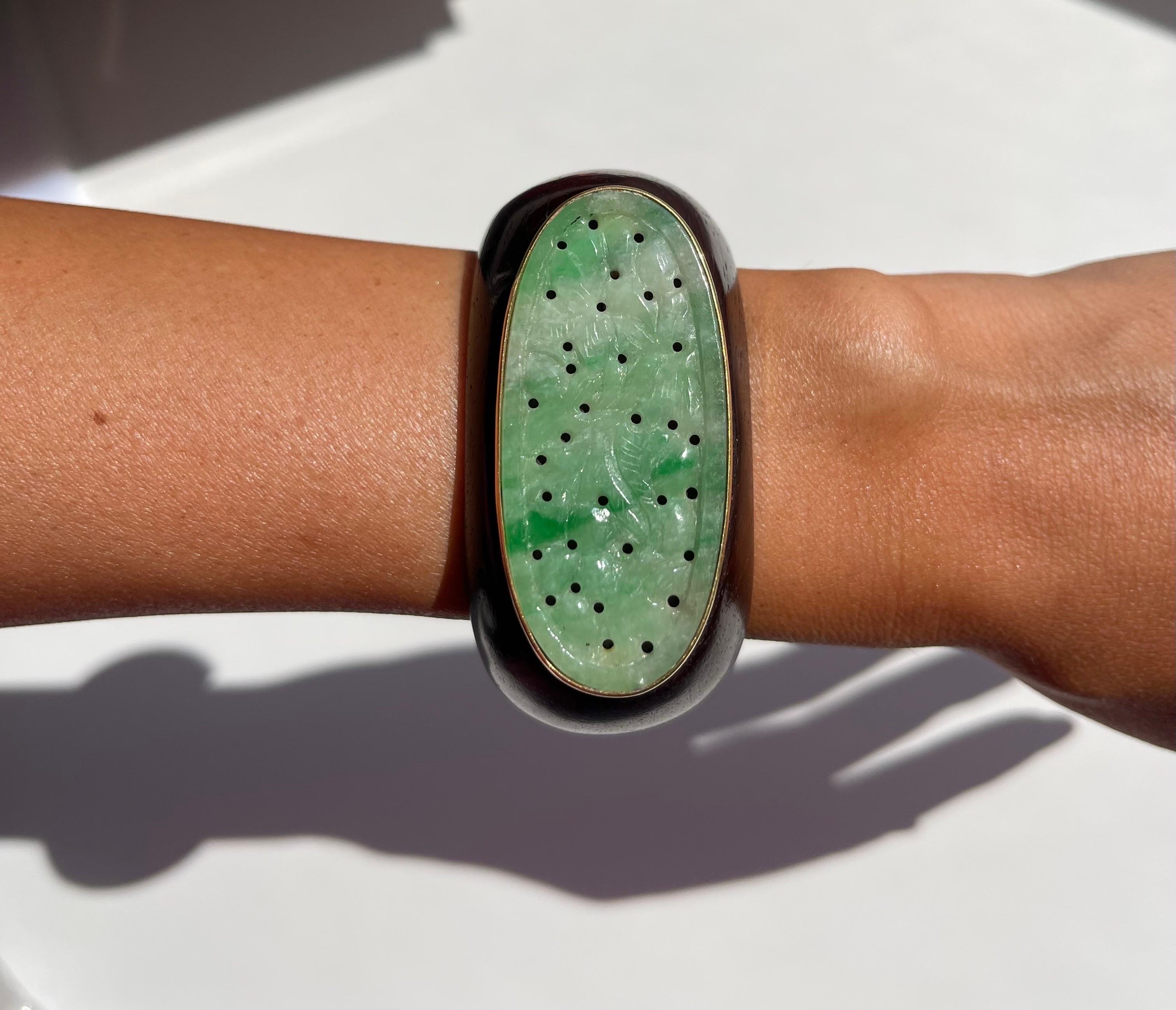 Dieses prächtige Armband ist ein Einzelstück, das aus einer ovalen, handgeschnitzten Jade besteht, die in 18-karätiges Gelbgold gefasst und an einem Holzarmband befestigt ist.  Traditionelle MATERIALIEN und einzigartige Akzente schaffen ein