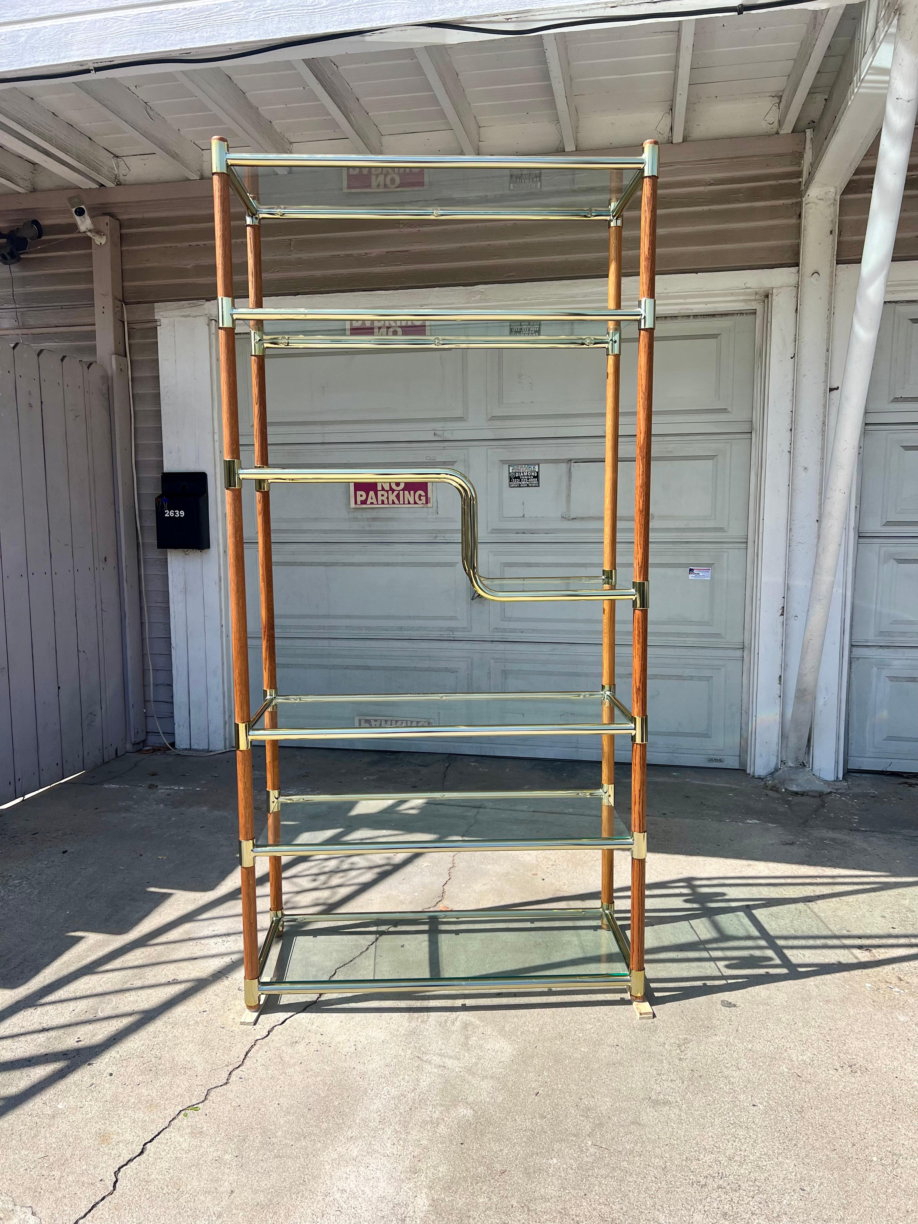 A beautiful etagere in the stye of Milo Baughman. Wood and brass frame with clear glass shelves. Can be disassembled. Overall excellent vintage condition. Some minor discoloration to brass at parts. No chips to glass shelves, but some scratches