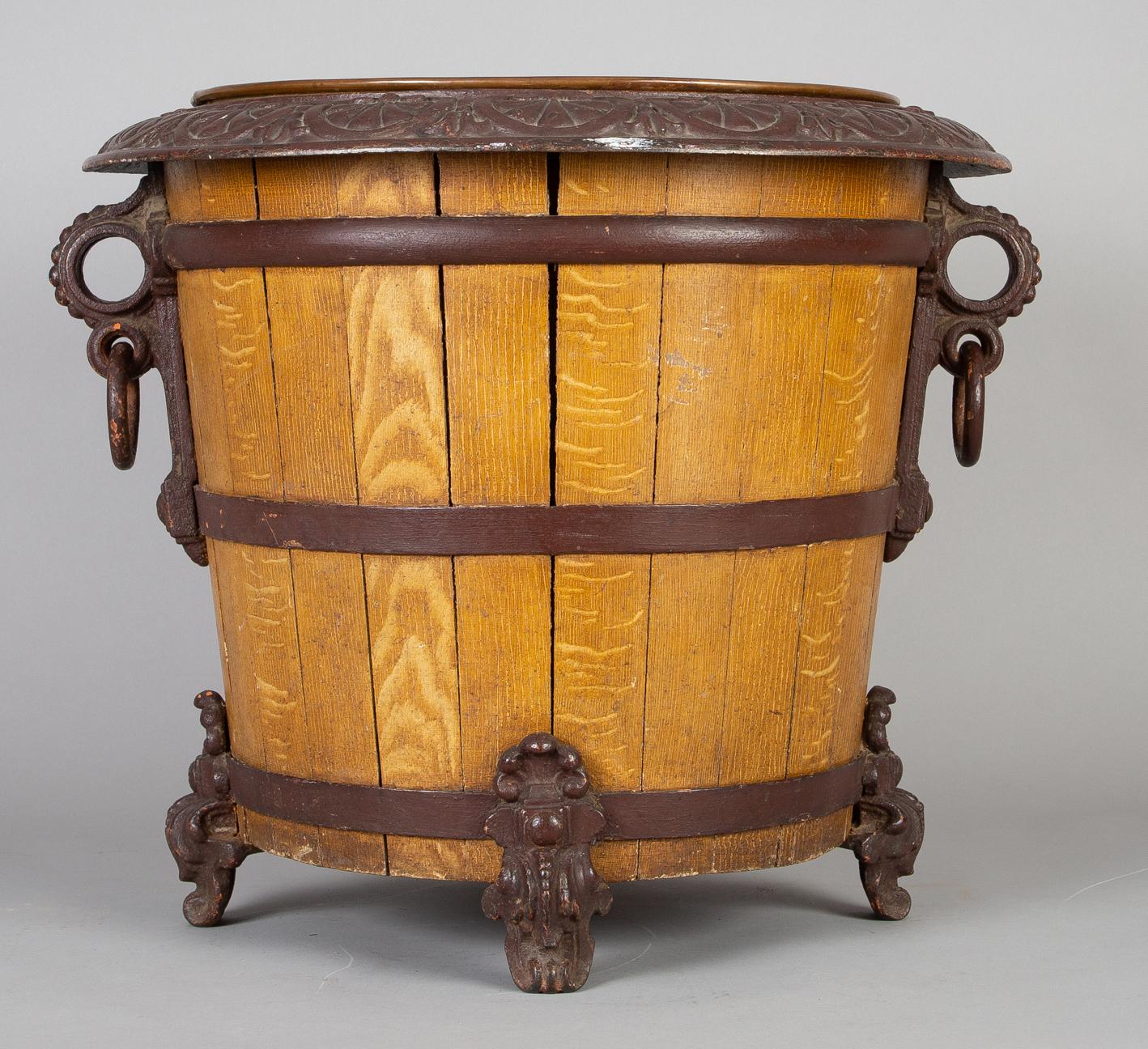 Cast iron and wooden jardinière or log container in barrel form with a copper liner, tapered wooden staves bound by cast iron hoops, decorative ring handles and feet.