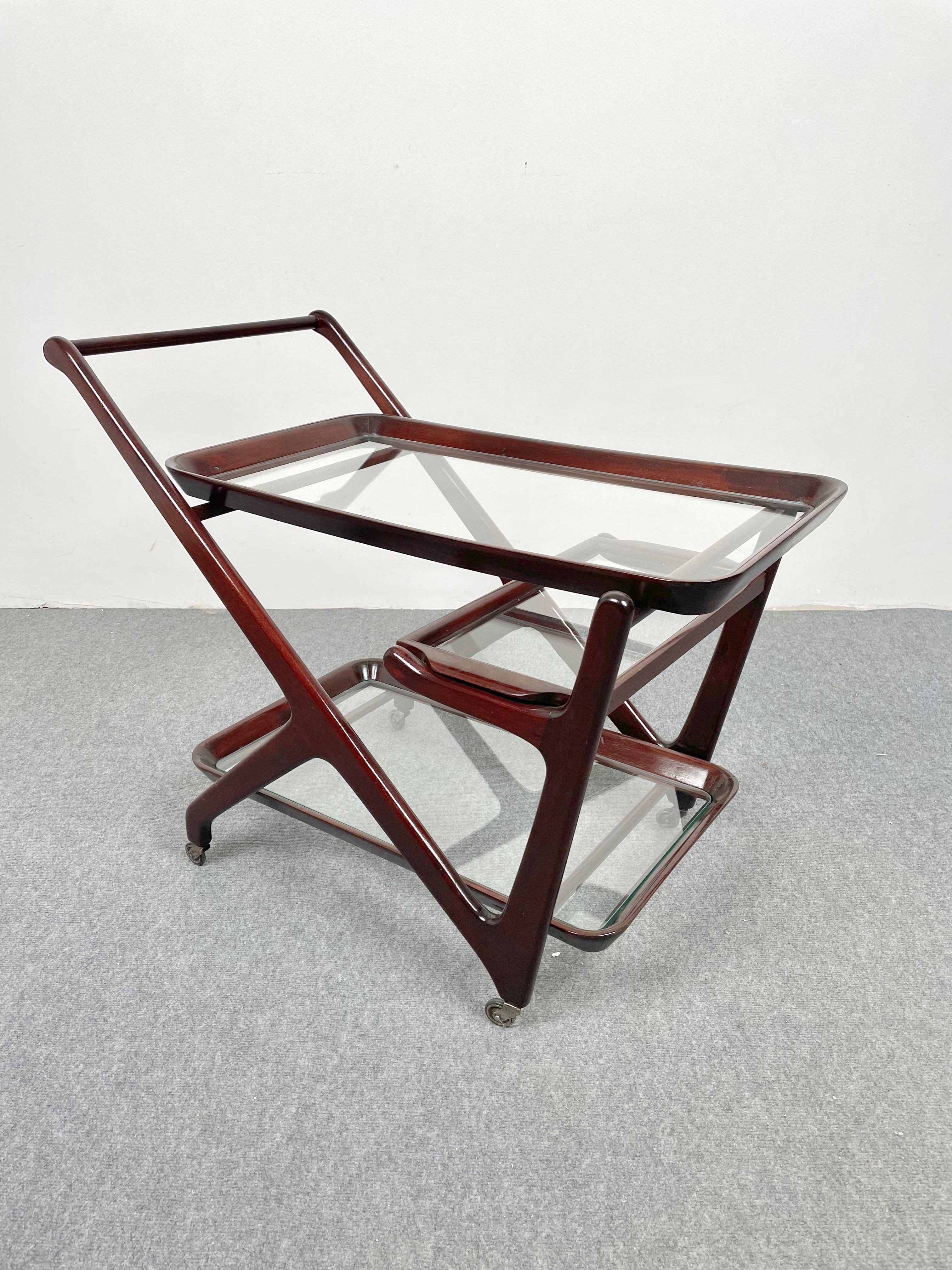 1950s serving bar cart featuring wood structure and three glass shelves by the Italian designer Cesare Lacca.
The little tray in the middle is removable.