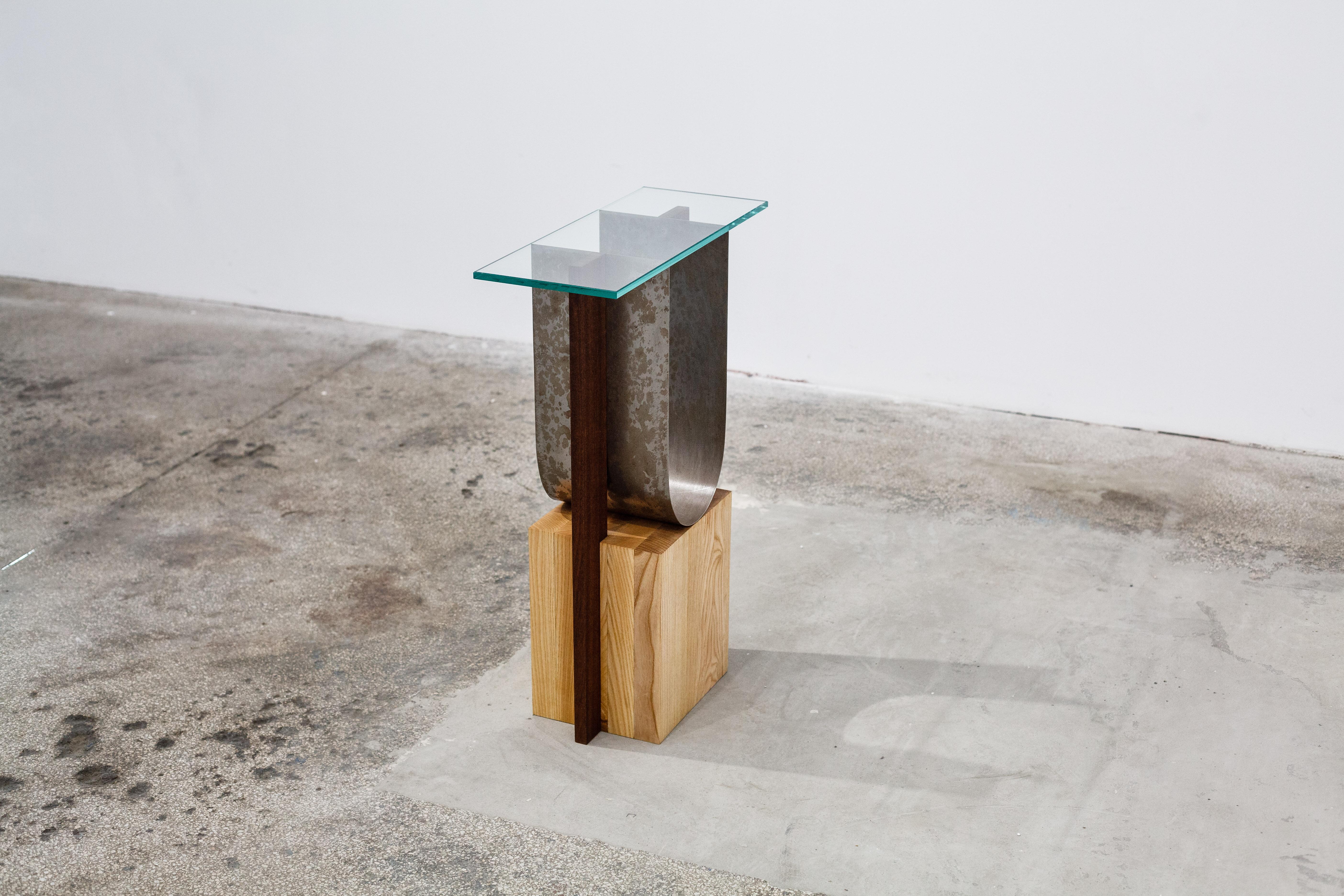 A side table that can also be used as a pedestal, made out of ash wood in combination with mahogany, metal and glass. The object  is part of a series named Form before function, where the focus is moved on the aesthetic of each object, rather than