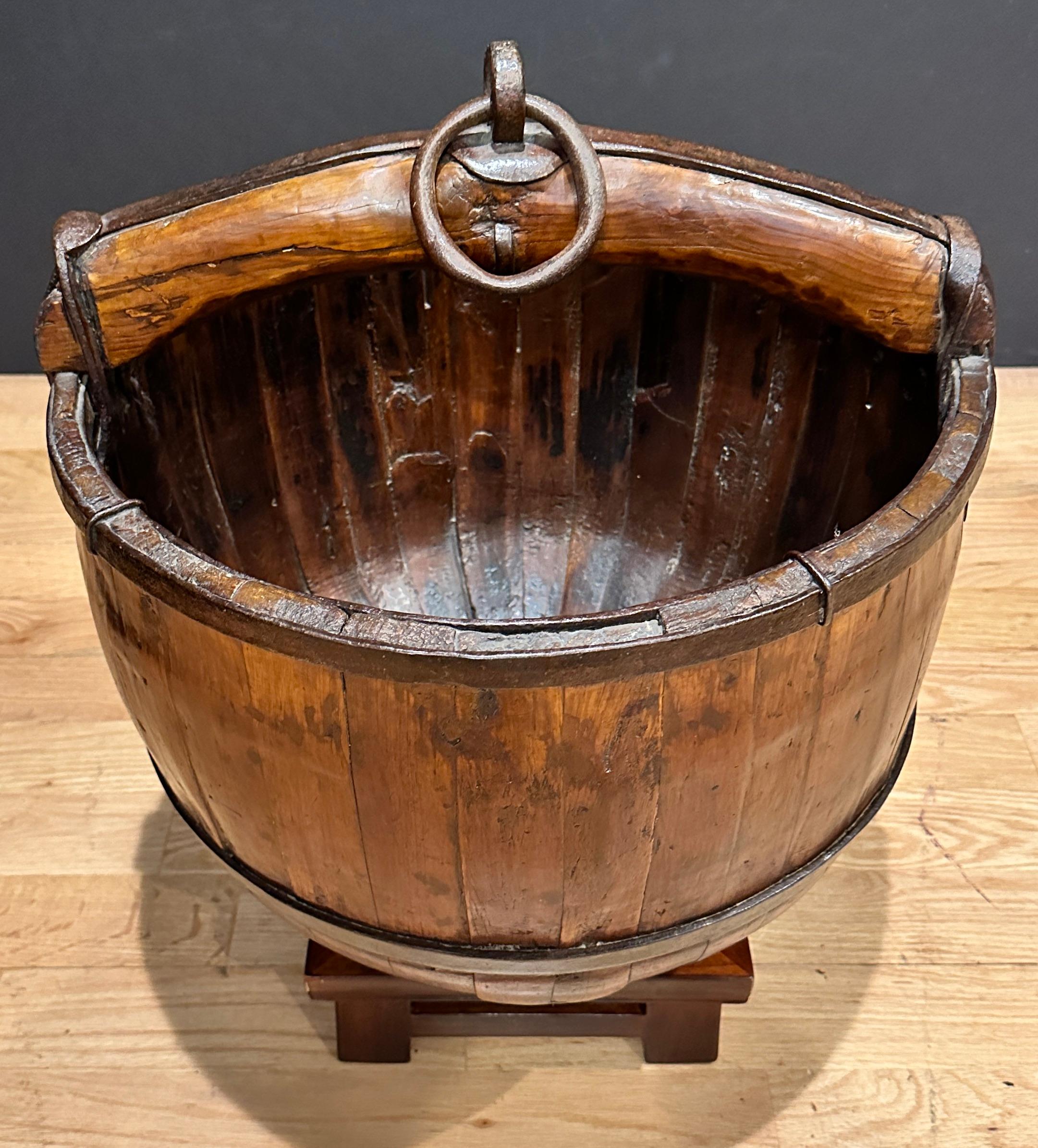 Antico secchio da pozzo cinese in ferro battuto forgiato a mano e legno di frutta. Di grandi dimensioni, seduto su un supporto in legno personalizzato. Può essere utilizzato come fioriera o come interessante decorazione.