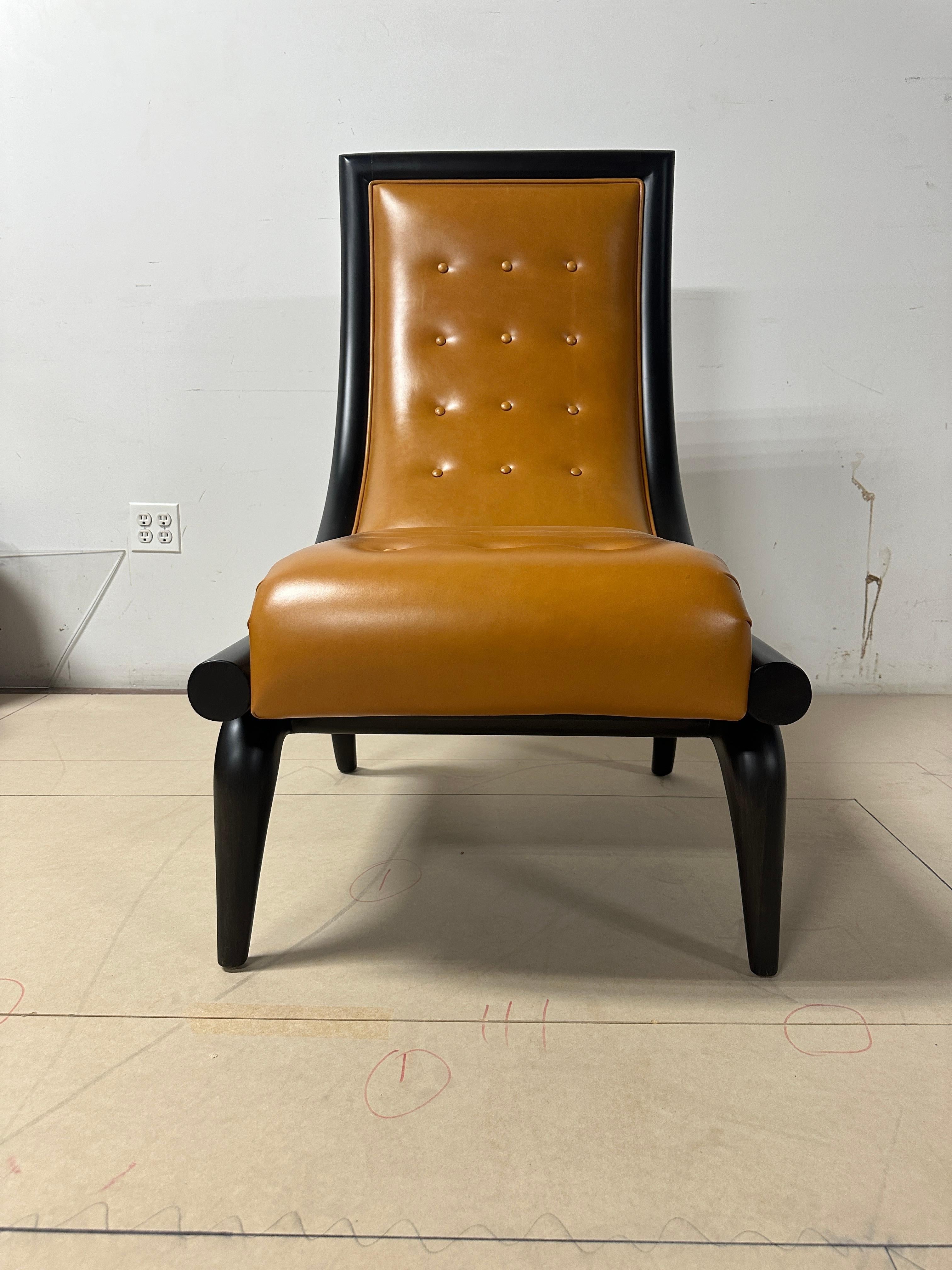 This exquisite lounge chair, designed by Juan Montoya, features a distinctive curved back and intricately hand-carved legs. Upholstered in rich, burned orange leather with elegant button-tufted detailing, it boasts a sophisticated dark grey-black