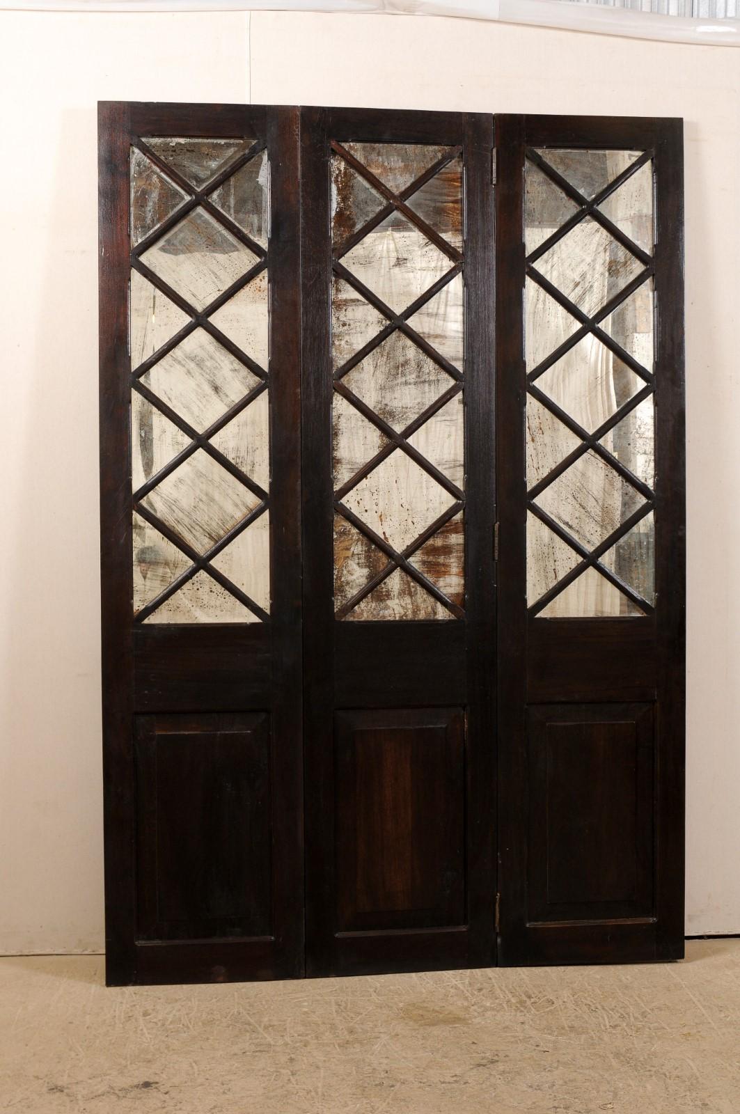 A free-standing mirrored three-panel folding screen room divider from the mid-20th century, Britain. This vintage screen features three-connected sections, each having a carved-wood raised panel at bottom, and a diamond-pattern lattice at top half