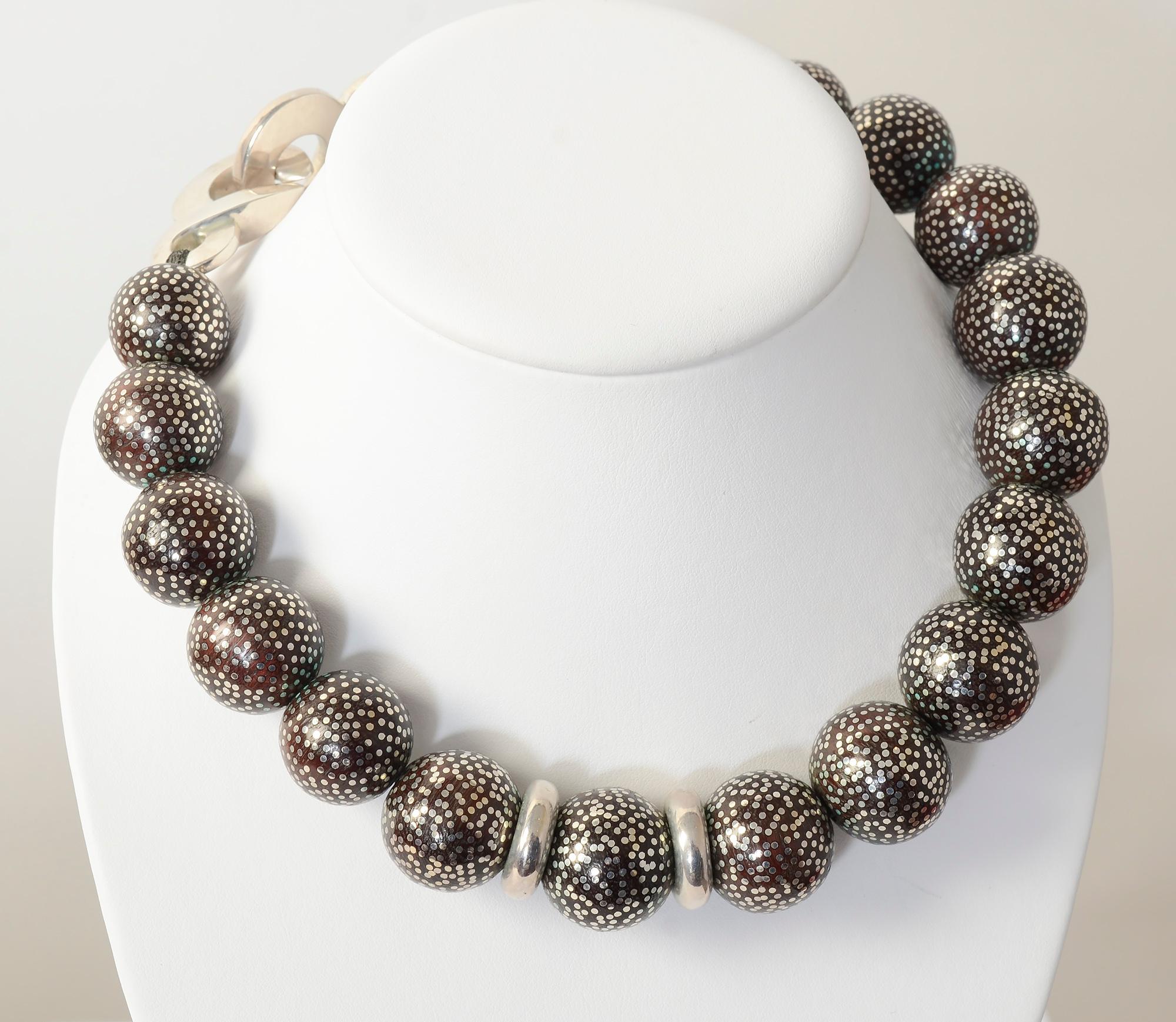 Dramatic wood bead necklace studded with tiny silver dots. The beads are approximately one inch in diameter but not exactly the same as they are handmade. The interlocking loops of the clasp are ornamental enough to be worn in the front or back.