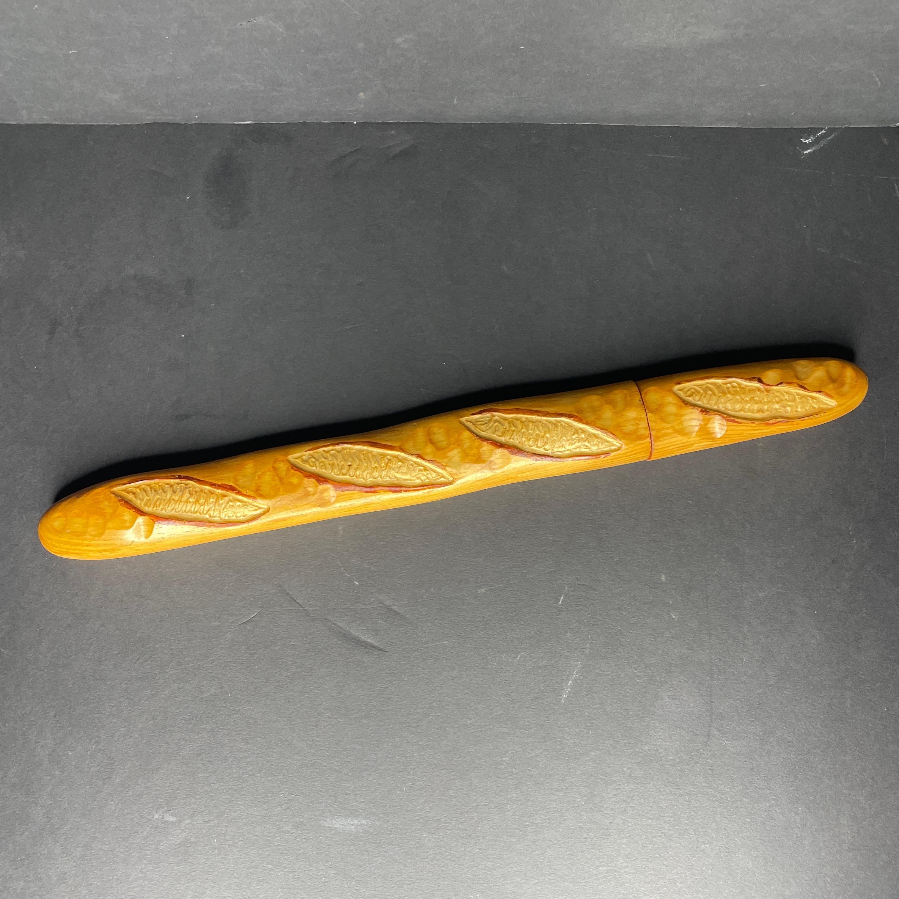 Grand couteau à pain en forme de baguette datant des années 80 et provenant de la coutellerie française Cuzin, fabriquée en France. 
Le manche est en bois, la lame est en acier inoxydable.
Estampillé dans le bois 