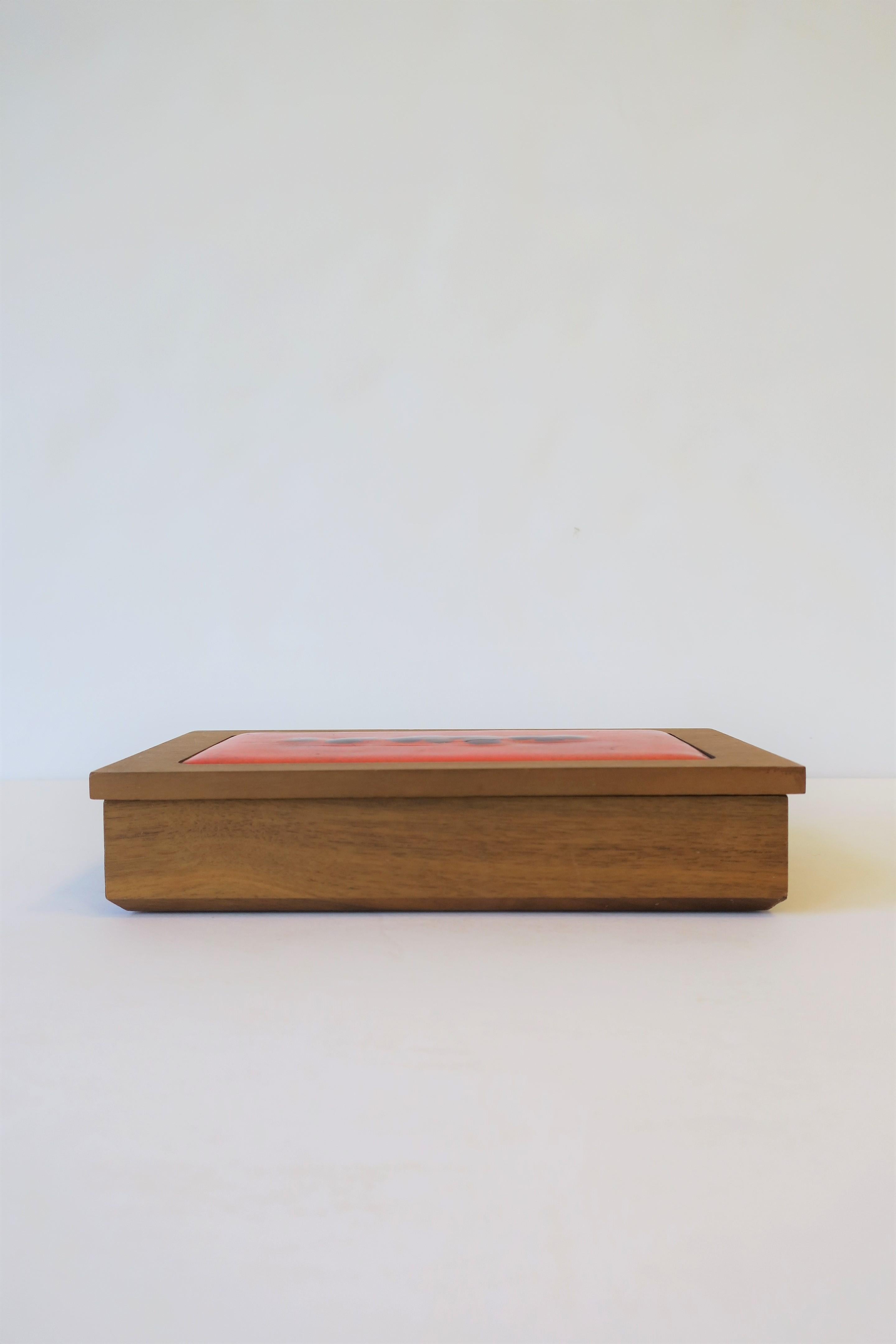 A beautiful Mid-Century Modern rectangular wood box with orange enamel or orange pottery and art glass decorative lid/top, circa mid-20th century, 1960s. Box could work well for small pieces like jewelry, trinkets, on a desk, or as a standalone
