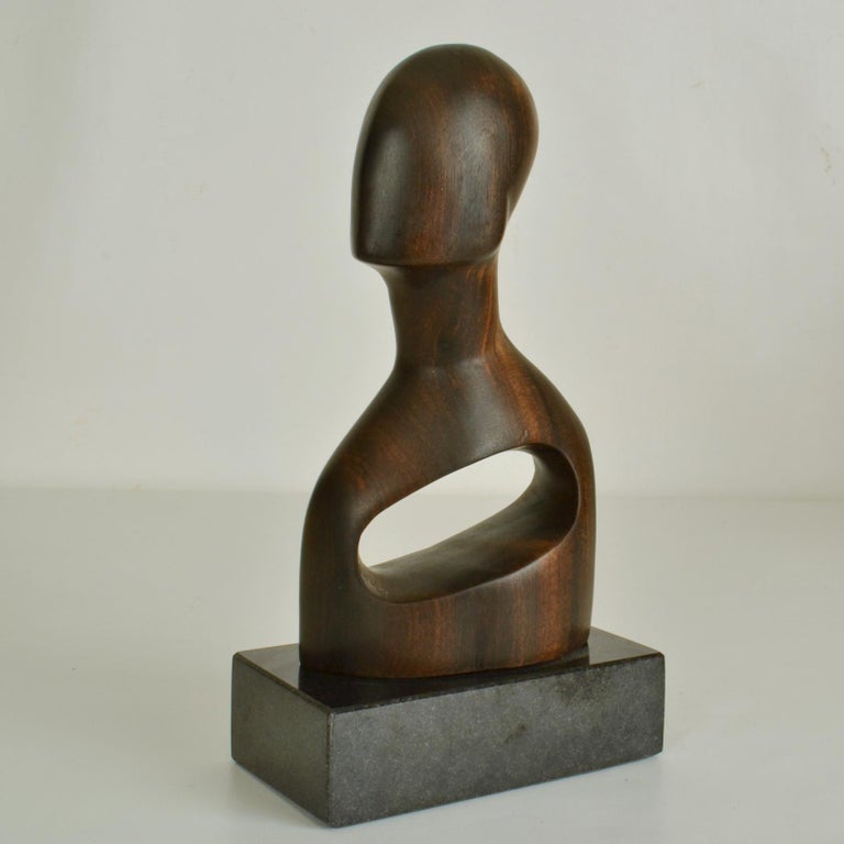 Abstracted bust hand carved in dark hardwood with a hole sits on a black granite base, 1970's. The abstract form of human representation breaks away from the idea of traditional form of the physical in the world of the real. It explores the