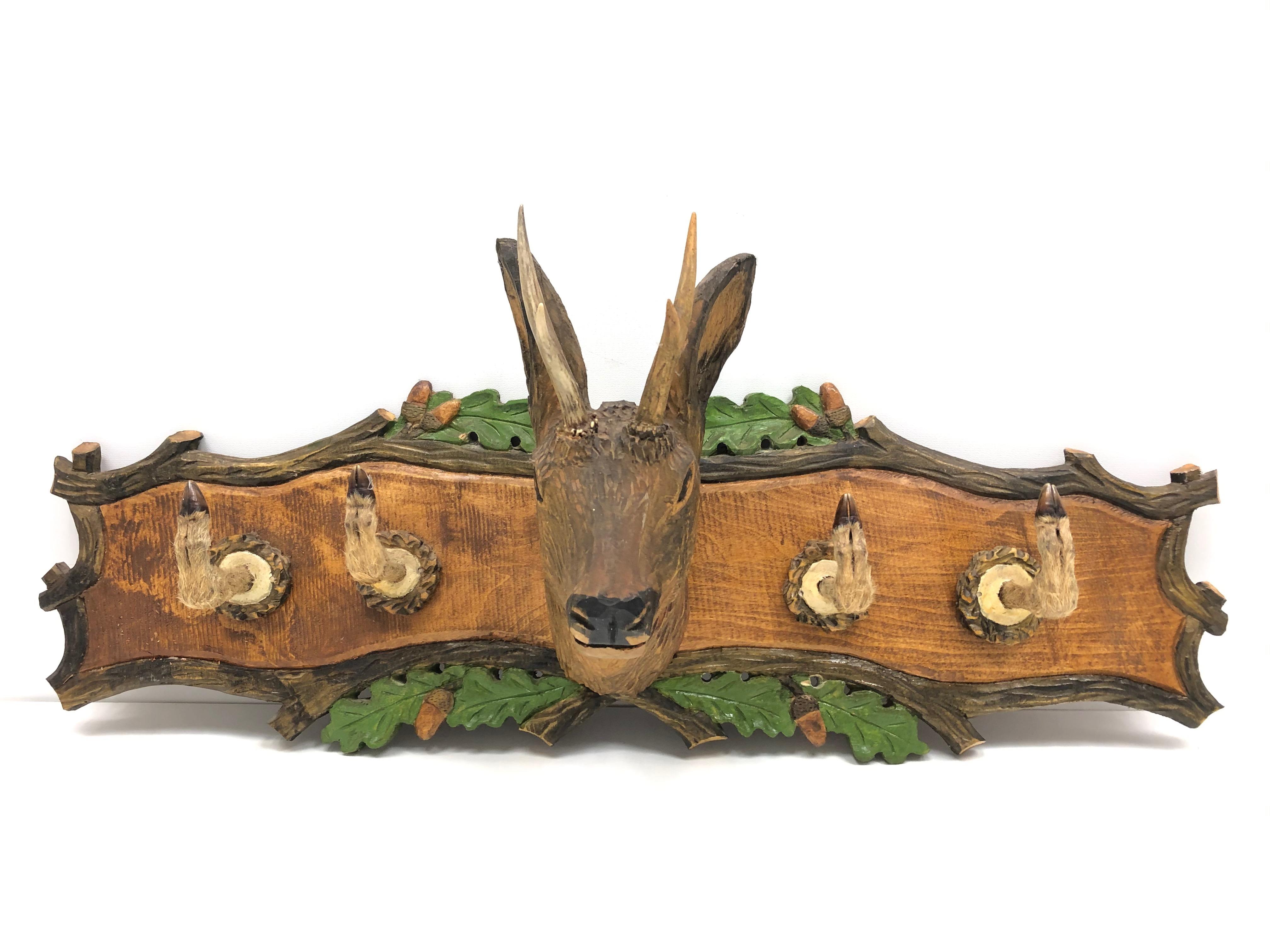 A beautiful whimsical 20th century German Black Forest carved head hat or coat rack with a small roe deer wood carved head, with four roe deer legs as hooks, mounted to a carved back with oak leaves. Nice addition to a hunters loge or just a man