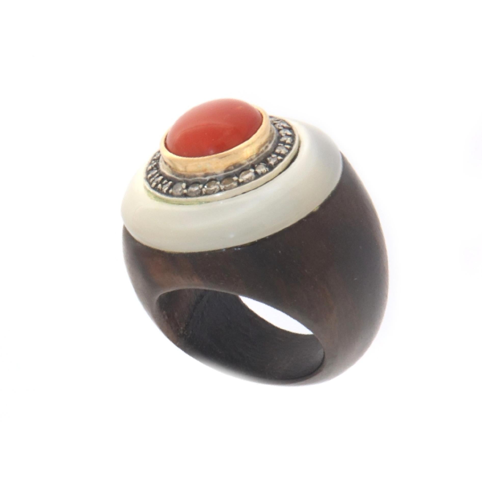 The stem of this particular ring was made entirely of wood, in the upper part a circular mother-of-pearl was applied which supports a small silver circle where diamonds are set which in turn support a natural red coral button surrounded by yellow