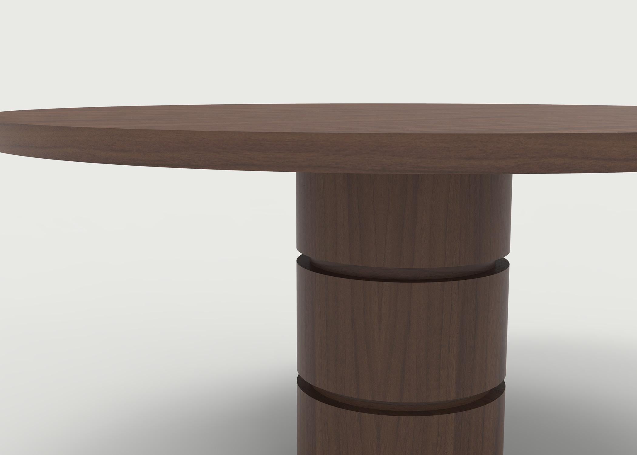 The Macon dining table shown in walnut wood with a solid top and special angled edge on top. The base is carved with special cut details to reveal an inside smaller base that can be made and finished in same or different wood and finish. All hand