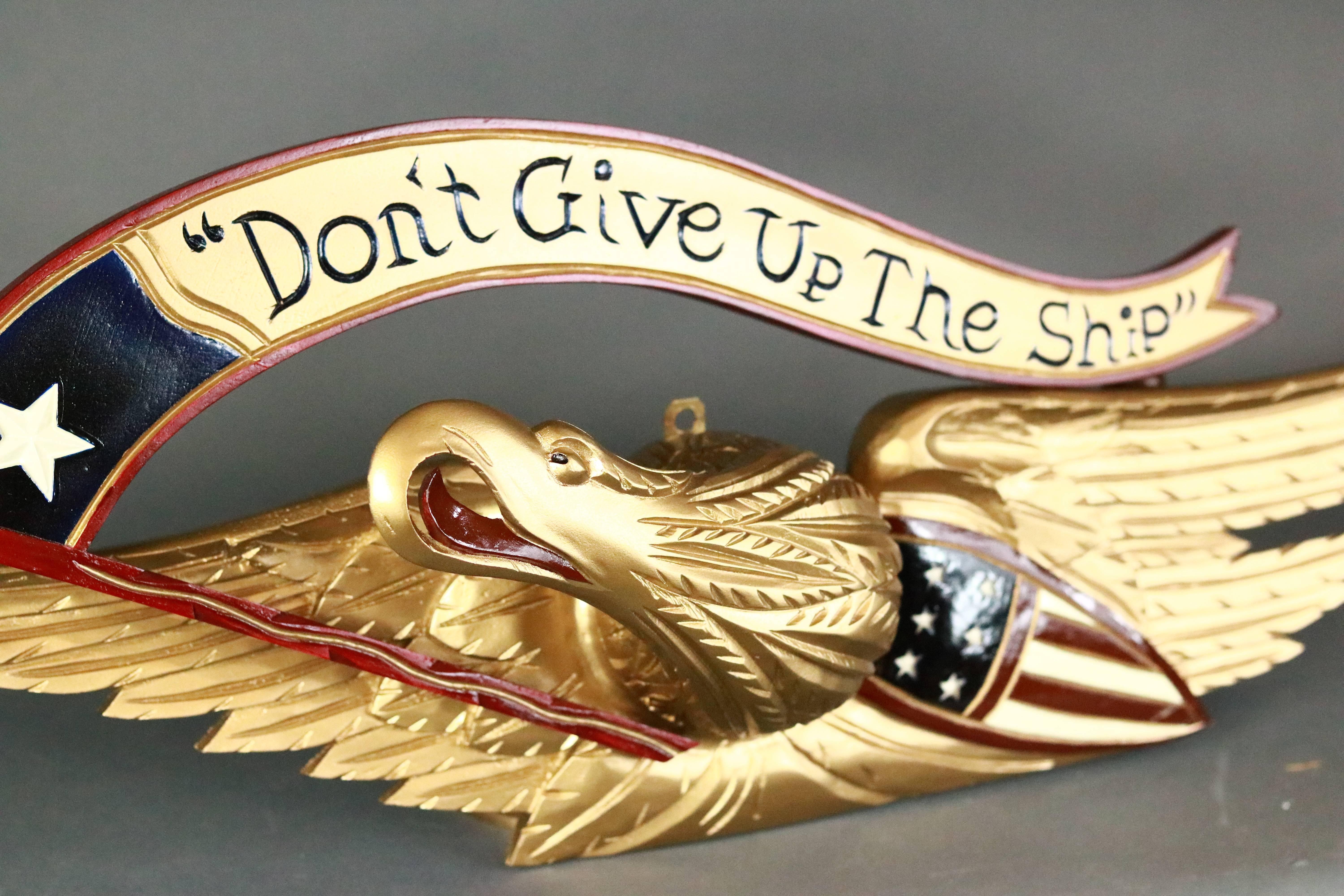 Carved wood eagle with gold finish. The eagle is clothing a banner reading Don’t Give Up The Ship and a red, white and blue patriotic banner.

Measure: approximate 31 x 16 x 7.