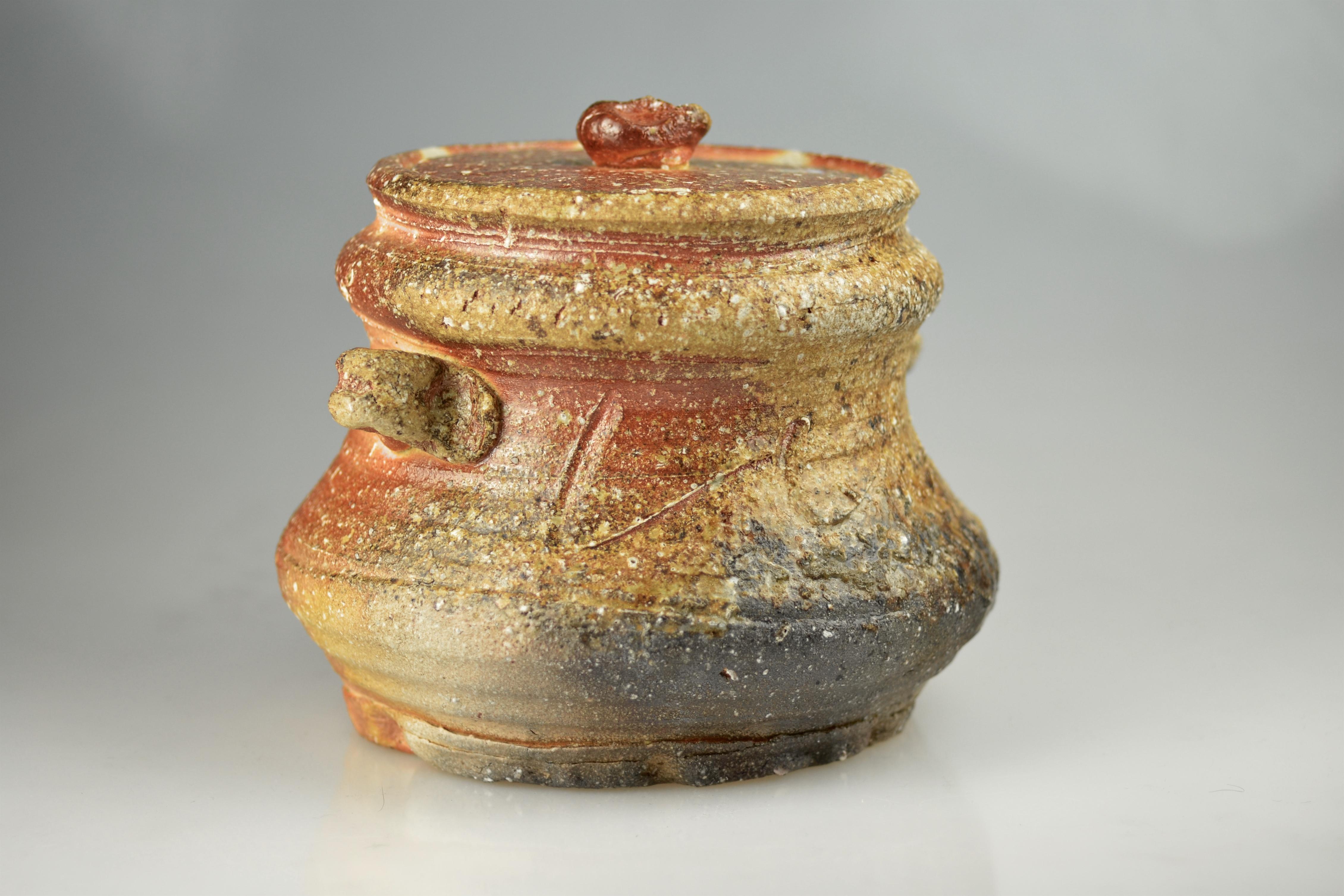 This spacious, ash-glazed Shigaraki jar with lid and handles was made by Takahashi Rakusai IV. He was born 1925 in Shigaraki and is probably the most famous Shigaraki potter. The Takahashi family is along with the Ueda family the oldest potter