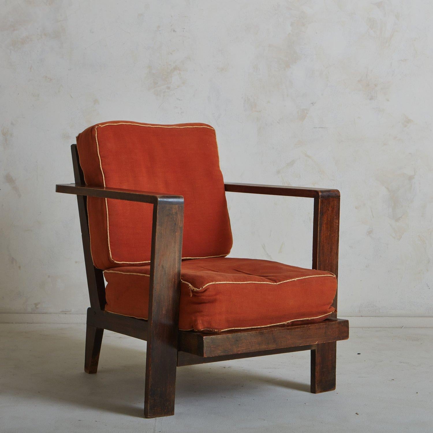A Vintage French lounge chair in the style of Rene Gabriel featuring a stately wood frame with a rich brown stain. The arms of the chair elegantly wrap around the ladder back. It has tapered back legs and two removable cushions in original coral