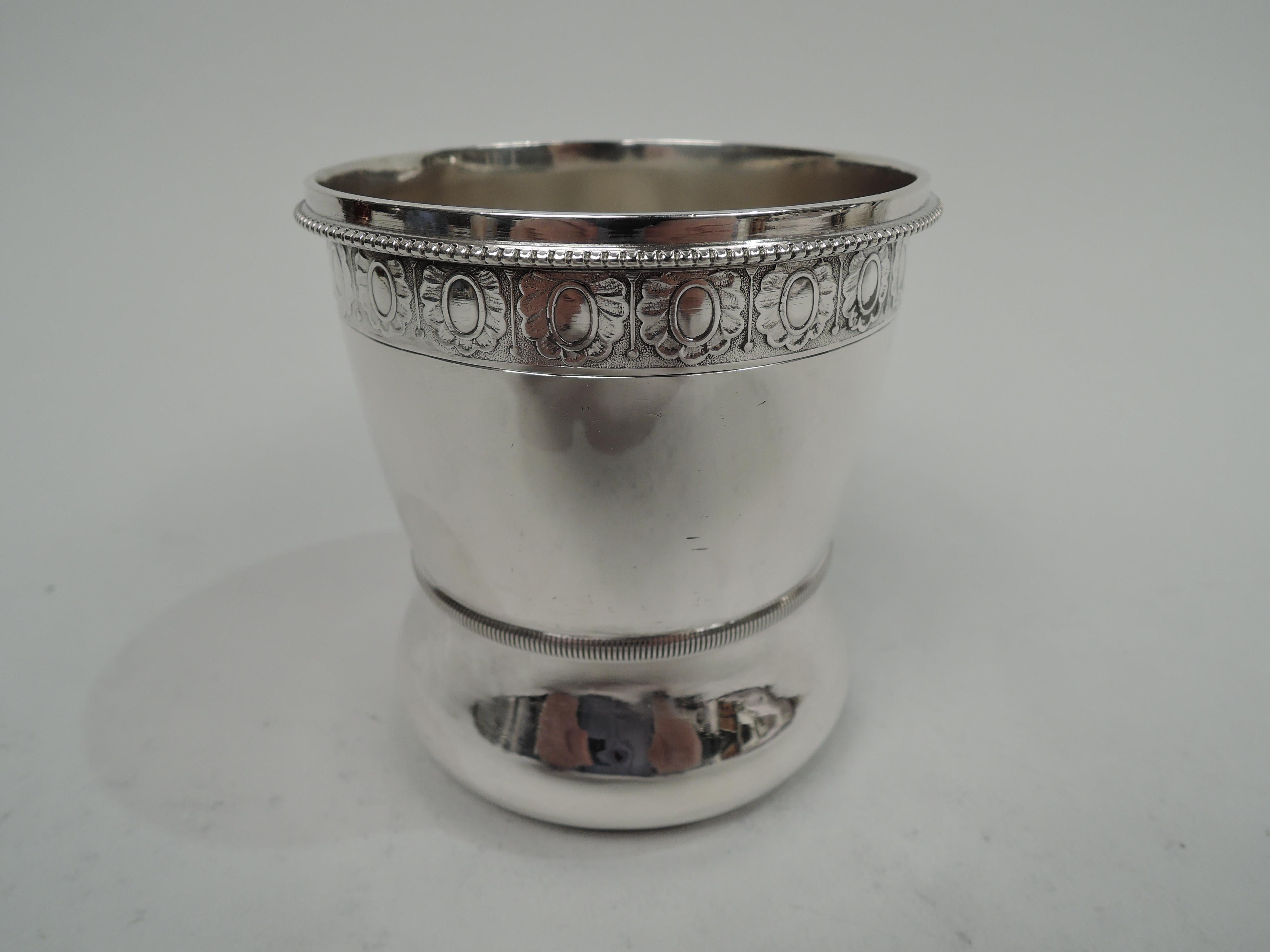 Aesthetic Classical sterling silver baby cup. Made by Wood & Hughes in New York, circa 1870. Wasted bowl with ribbed girdle and leaf-mounted and capped c-scroll handle. Beaded rim and low-relief border flower-head and dart motif on stippled ground.