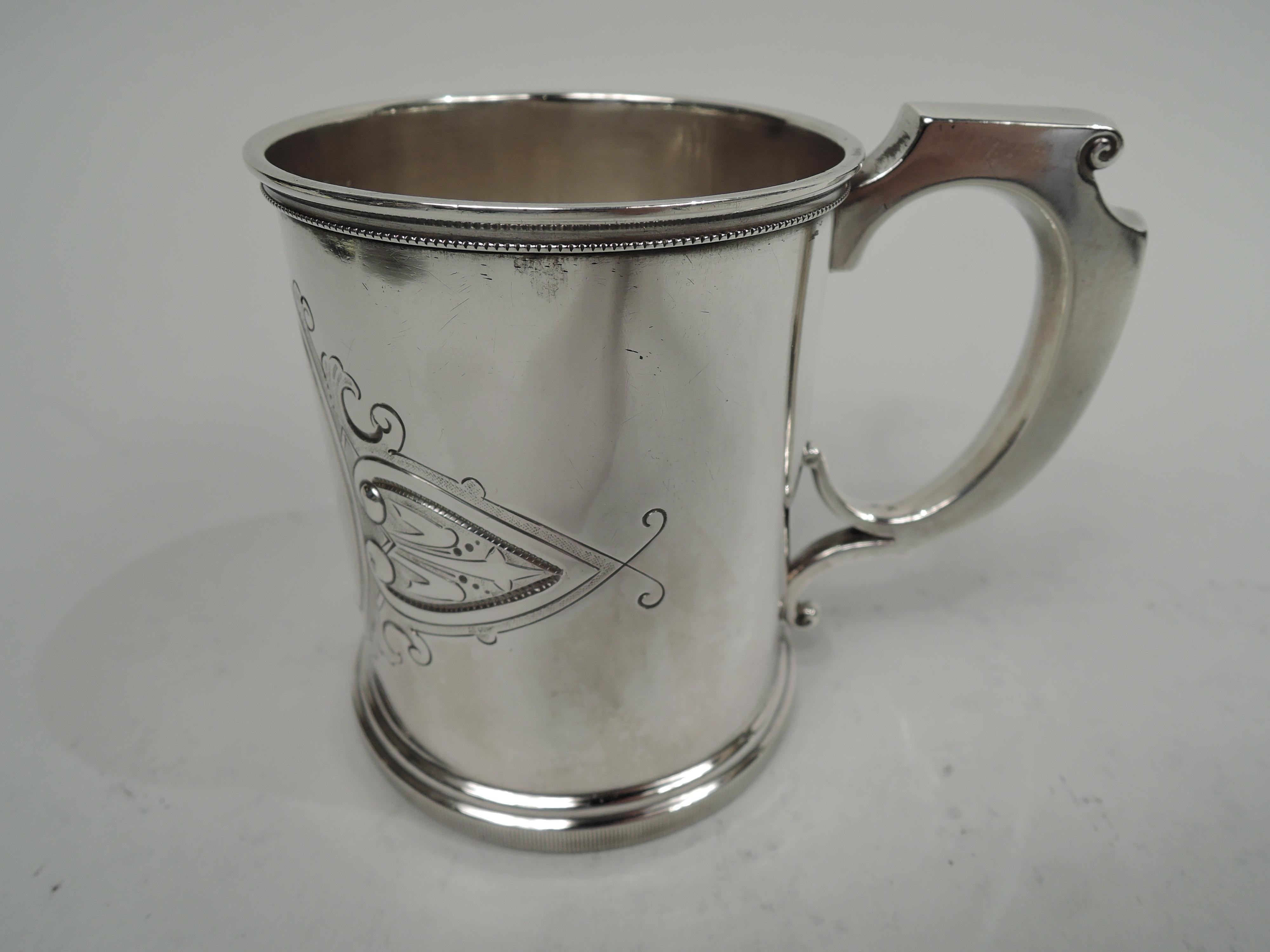 Victorian Classical sterling silver baby cup. Made by Wood & Hughes in New York, circa 1870. Straight sides and split mounted scroll handle with volute scroll cap. Chased leafing scroll oval frame (vacant) in stylized leaf and scroll surround with