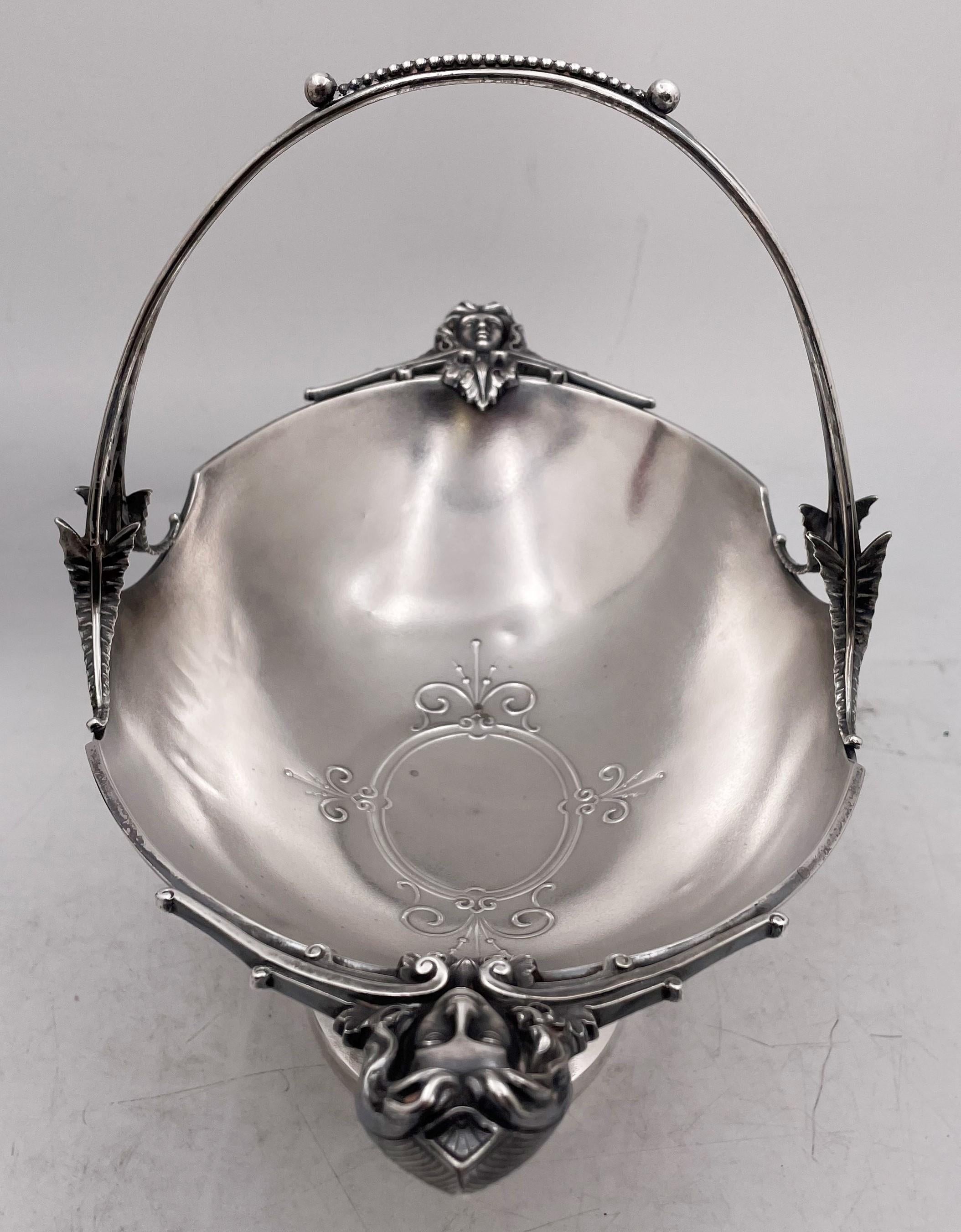 Wood & Hughes sterling silver basket or bowl with a fixed handle, showcasing an elegant design, with female faces on either end as well as stylized motifs on the handle, in the bowl, and above the base. It measures 13'' from in length by 7'' in