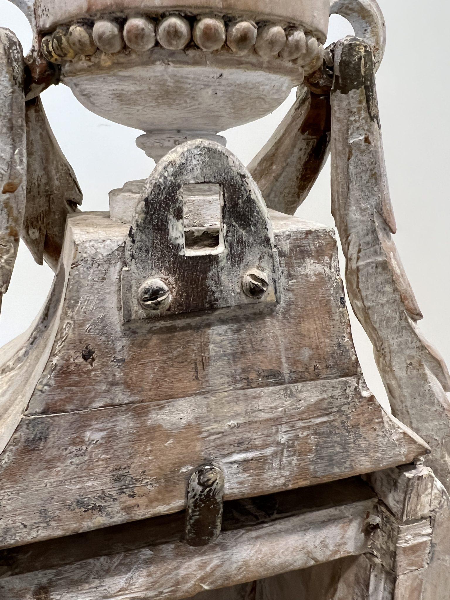Reloj de chimenea de madera lavada blanca muy ornamentado con detalles dorados. La cara está detrás de una puerta de cristal funcional con pestillo. La parte superior está coronada por una urna con una guirnalda de laurel en cascada que cae a ambos