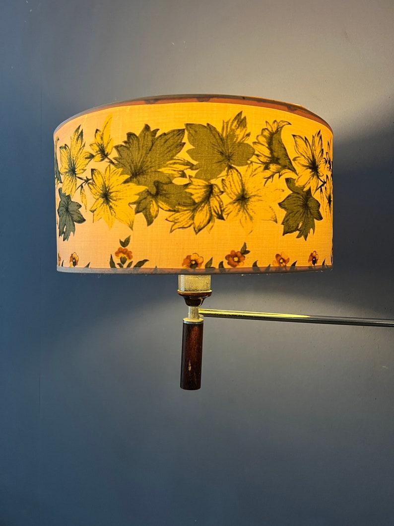 Classy mid-century swing arm wall lamp with textile flower patterned shade and wooden elements. The lamp has a beige and green shade and the arm consists of metal and wood. The lamp requires an E27/26 (standard) lightbulb and currently has an