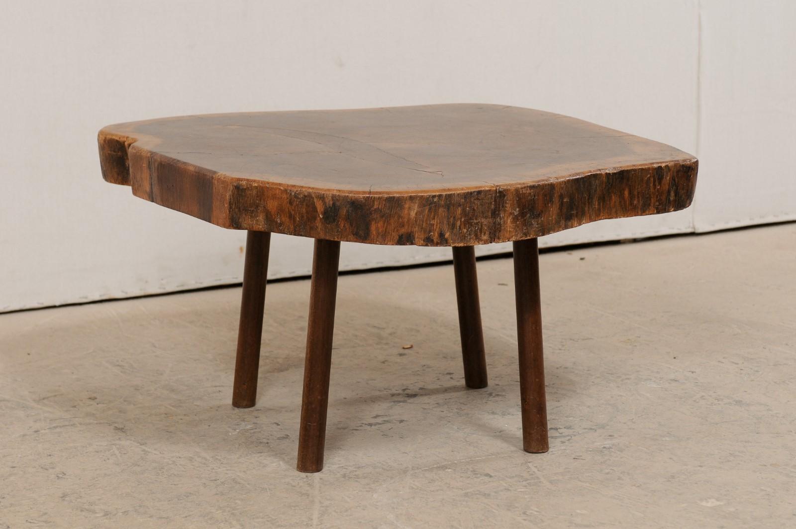 A smaller-sized European wood slab top coffee table from the early 20th century. This antique table from Europe features a natural wood slab top, with smoothed edges, which has been raised on four rounded legs. The table top displays it's