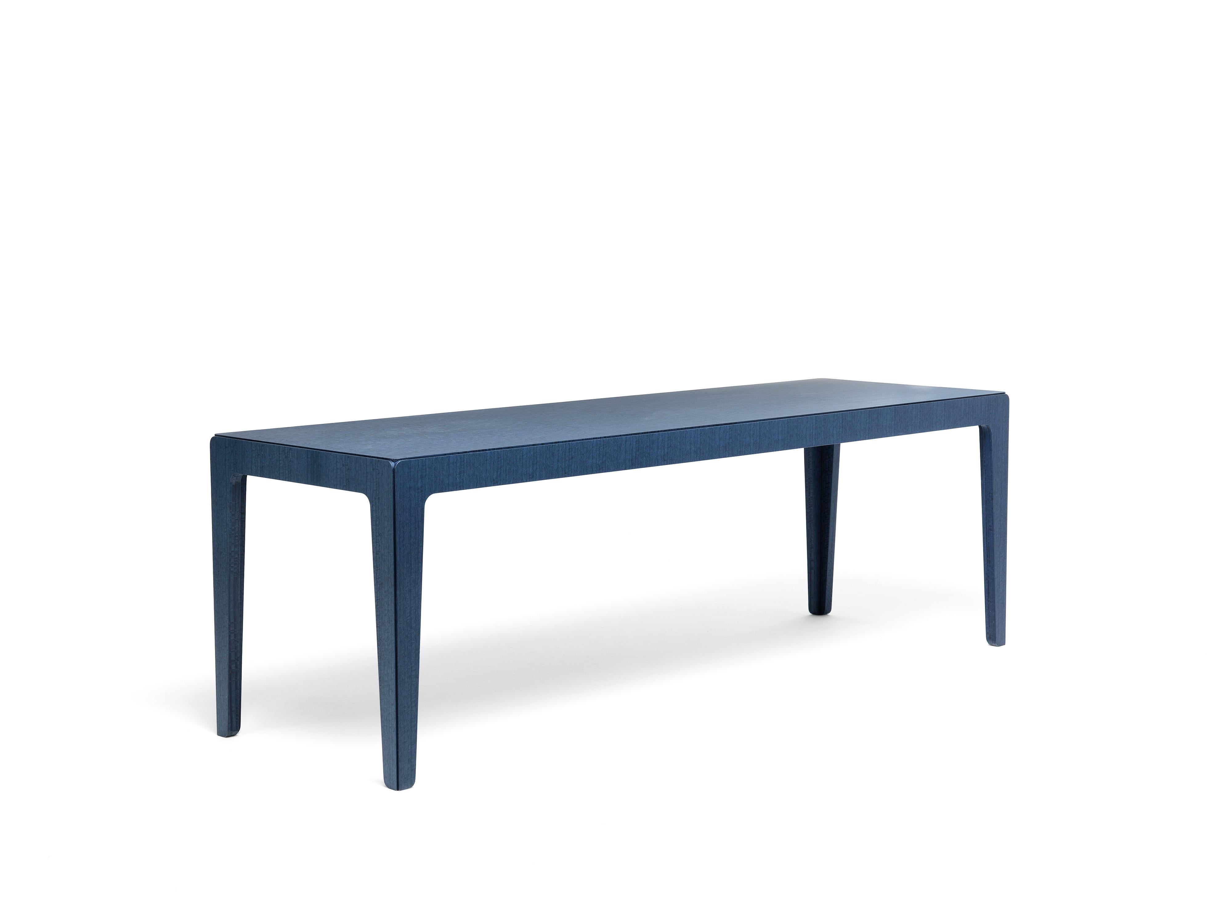 Une famille de tables à 4 pieds en MDF recouvert de placage d'eucalyptus teinté bleu. Grâce à une astuce simple, la table, qui est en fait l'assemblage de cinq pièces, semble sculptée dans un bloc solide. Les quatre éléments latéraux, une fois