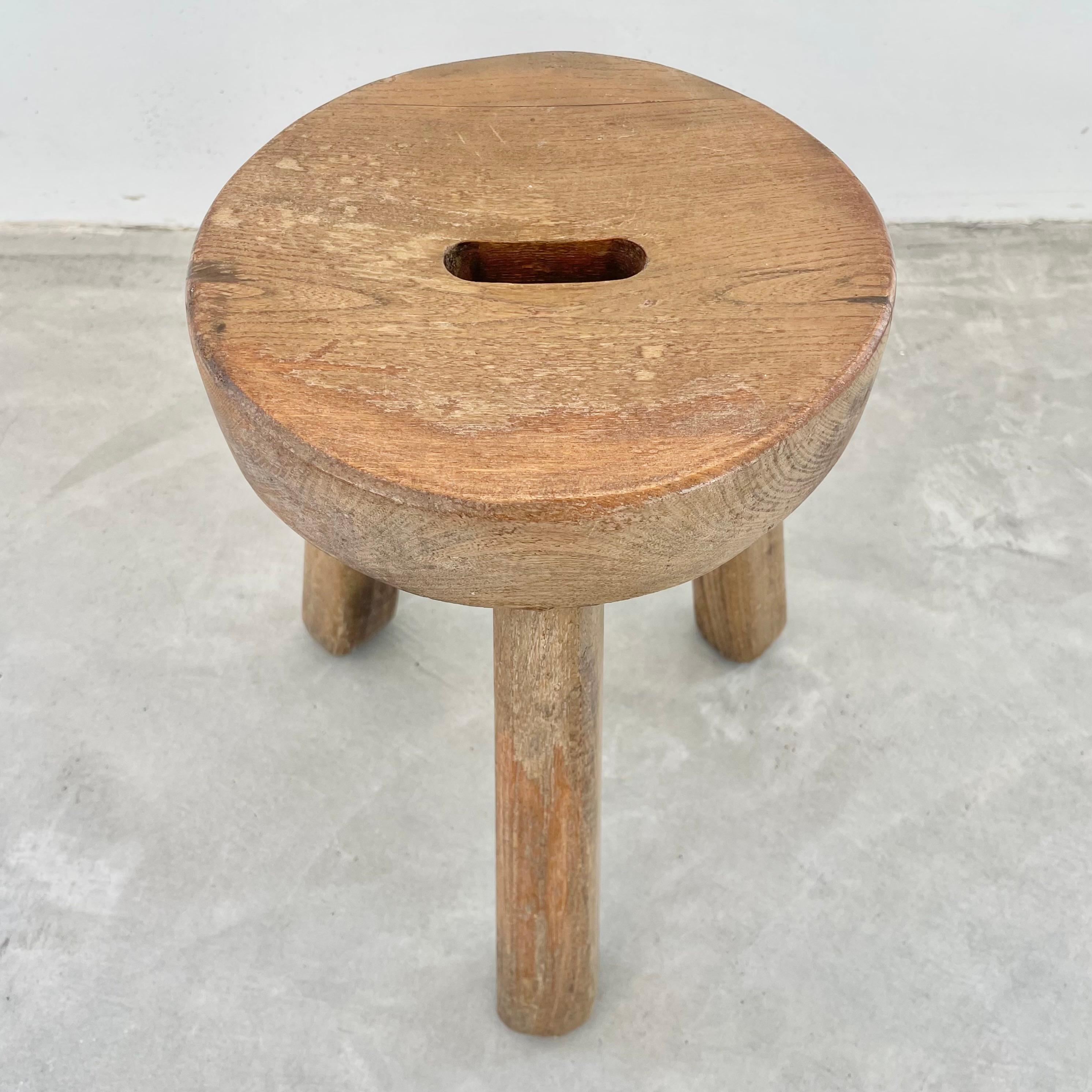 Unique tripod stool made in France, circa 1970s. Substantial and chunky round seat with three sturdy club legs that taper out at the bottom. Oval hole cut out in the middle of the seat as a handle. Perfect patina and age to this piece. Functional