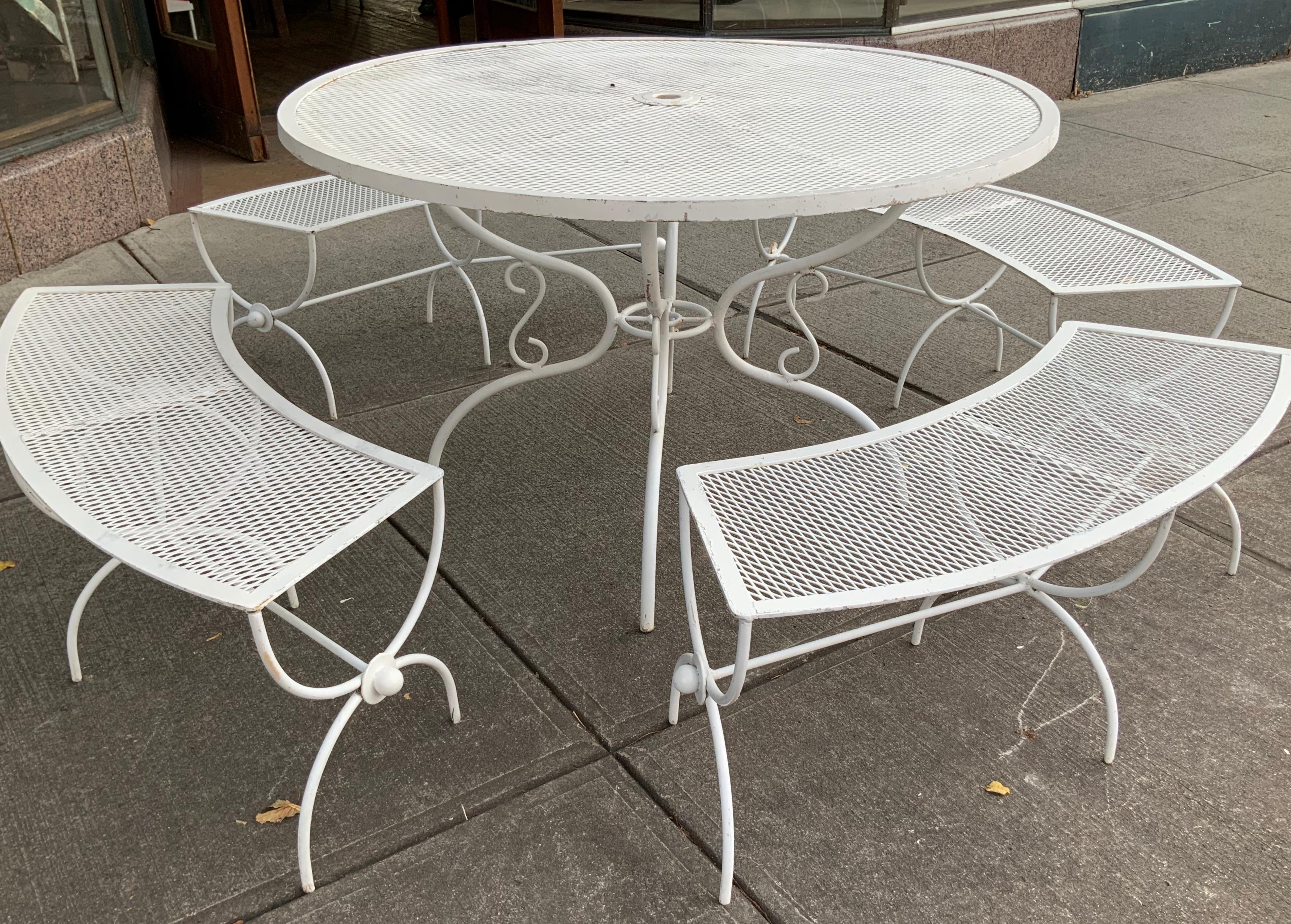A beautiful vintage 1950s wrought iron dining set with a round table and set of four curved benches. The table with a scrolled base and the benches have Curule bases. In its original white painted finish, which shows average wear for the age.