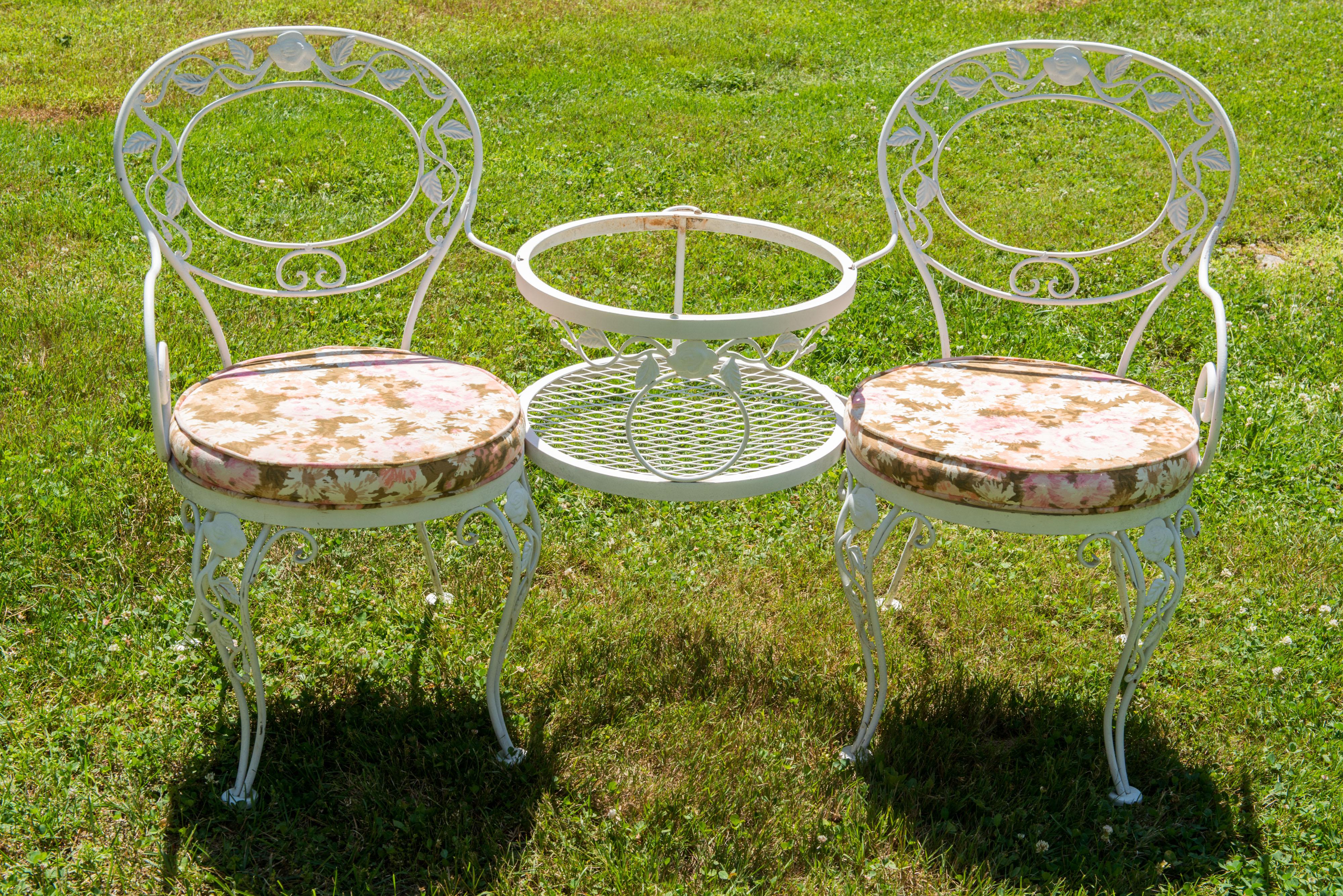 This is the classic vintage Woodard Chantilly Rose wrought iron Tete a Tete - a pair of attached arm chairs with a small round glass top table between them. At the back of the table there are two iron rings to accommodate a shade umbrella. The glass