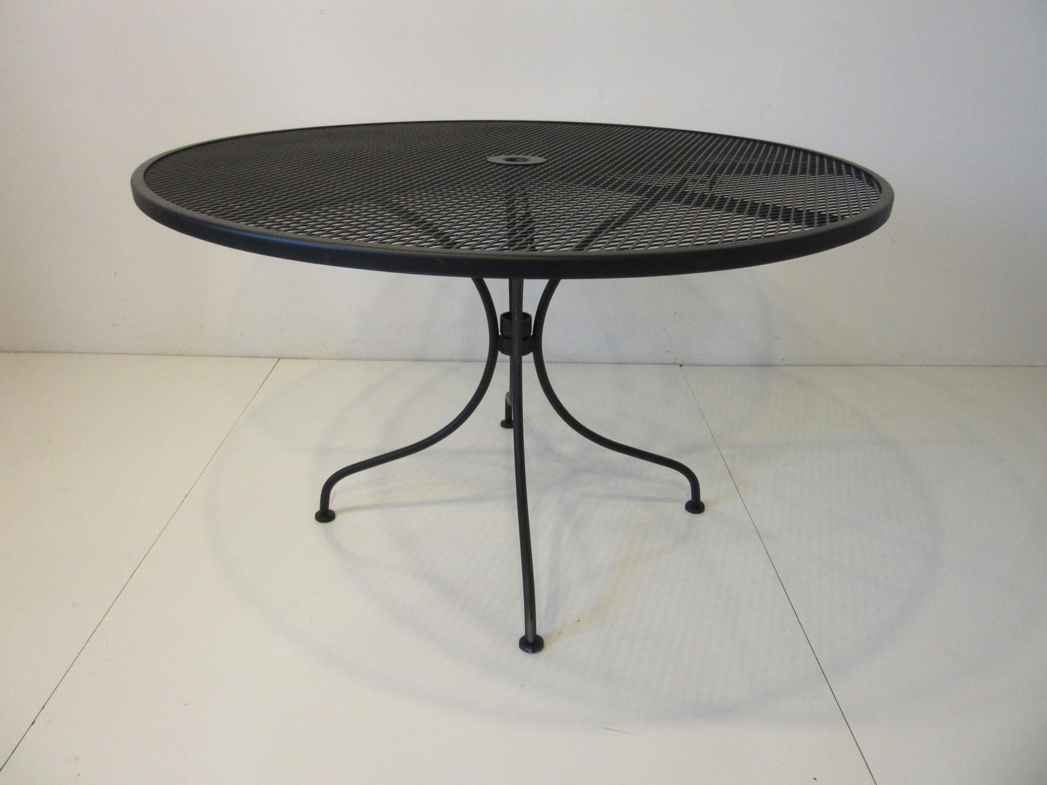 A satin black restored metal mesh dining table with center hole for a large table umbrella, designed by John Woodard. Very well crafted and manufactured by the Woodard Furniture company Owosso Michigan, this table has a two piece base and separate