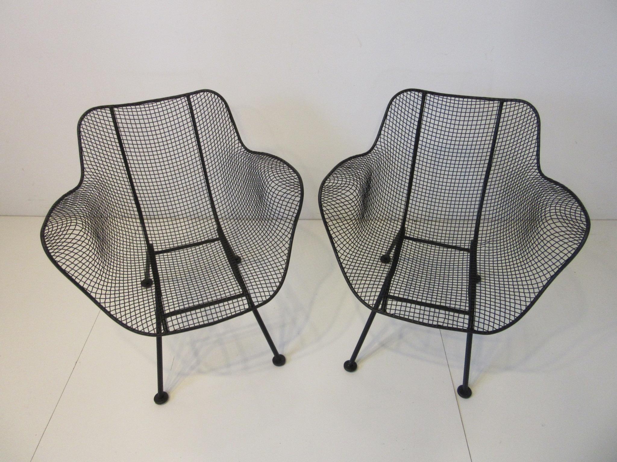 A pair of molded wire mesh arm chairs in the lower lounge height for comfort with the protective foot pads to the bottom of the feet. Refinished in the original satin black color being professionally dipped, primed and painted for indoor, outdoor or