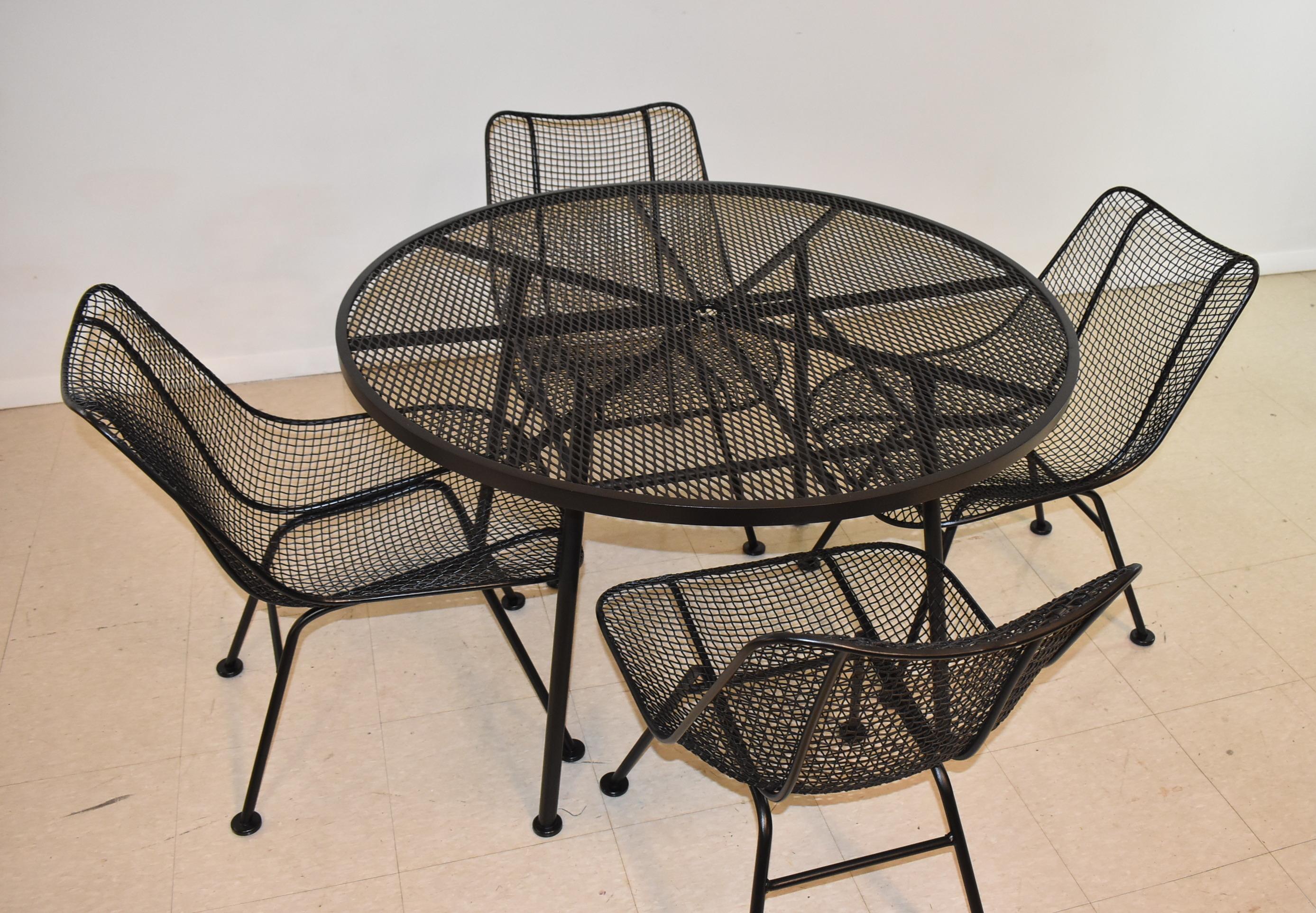 Classic mid-century modern Woodard patio set with a round table and four Sculptura chairs of black gloss painted steel. Table has umbrella hole and is 41 1/2