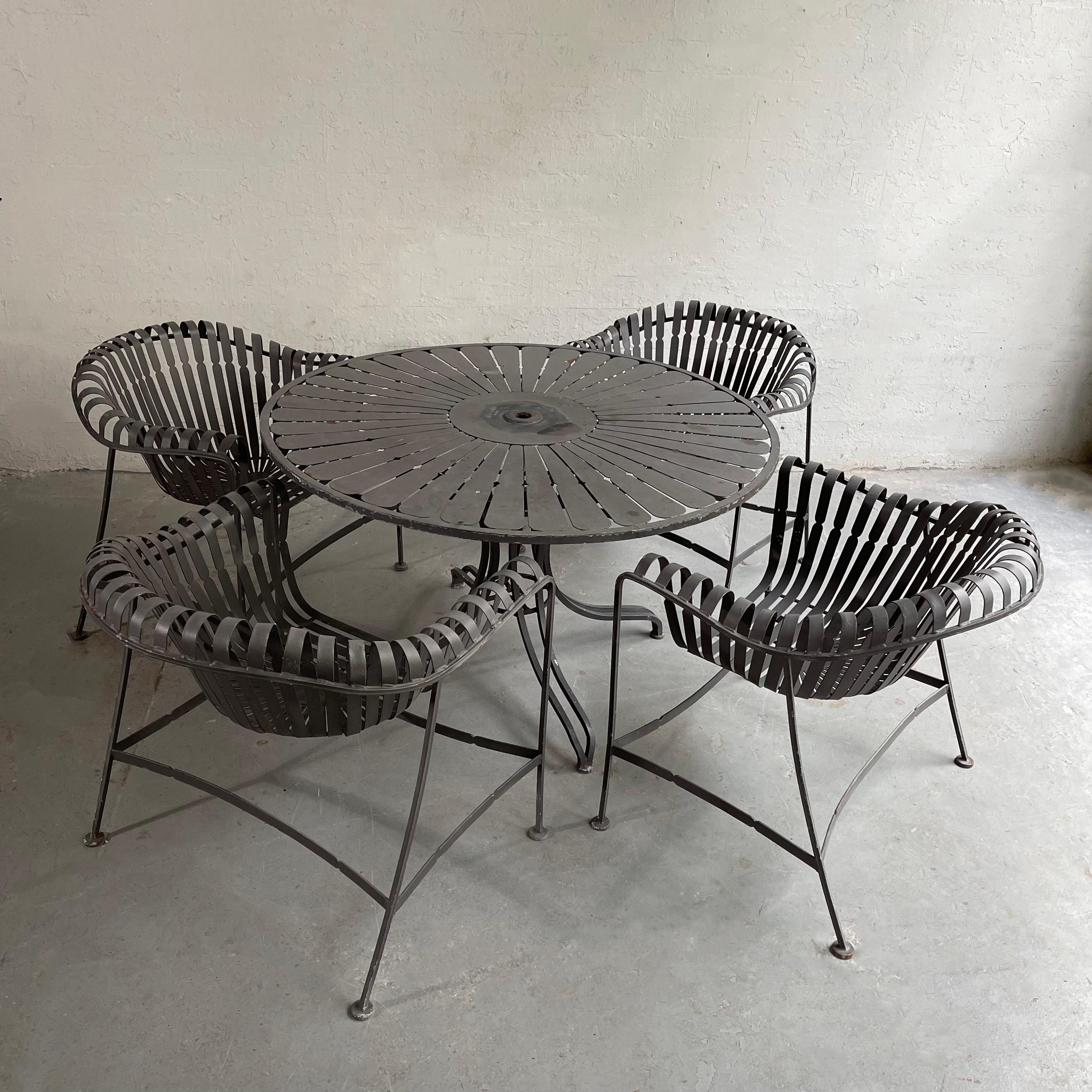 Midcentury, painted wrought iron, garden, patio, dining set with round, sunburst table and four strap iron armchairs by Woodard Furniture is also reminiscent of French garden furniture in the manner of Francois Carre´. A lovely, unique dining set