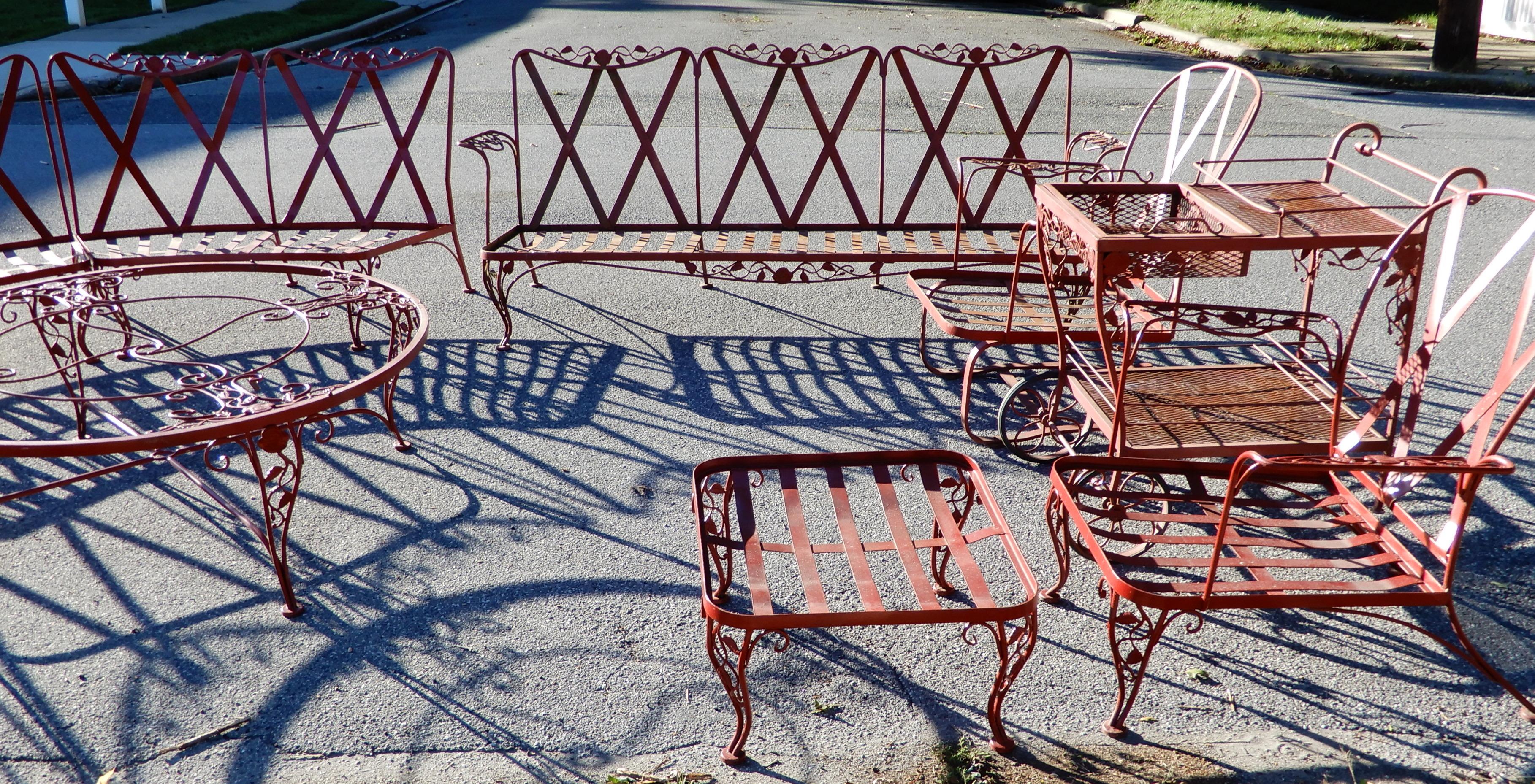 A vintage Woodard Chantilly rose wrought iron patio set. This extensive Woodard patio set consists of a 1-piece sofa, a curved 3-piece sofa, a 48” round glass top coffee table, a footstool, a pair of armchairs, a teacart, and a glass top side table.