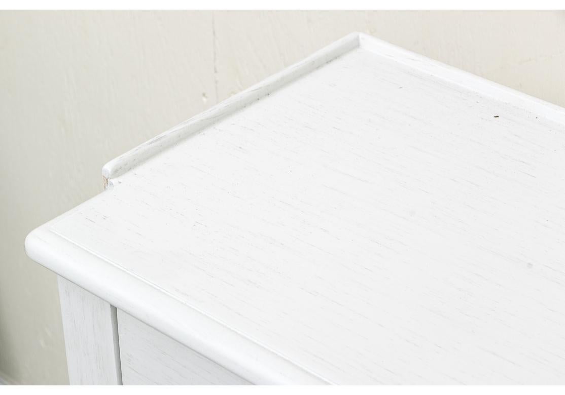 Une longue table console finie en peinture blanche avec une garniture à galerie basse sur trois côtés, quatre tiroirs courts avec des poignées en lucite au-dessus d'un espace de rangement ouvert. La console repose sur six pieds effilés qui sont