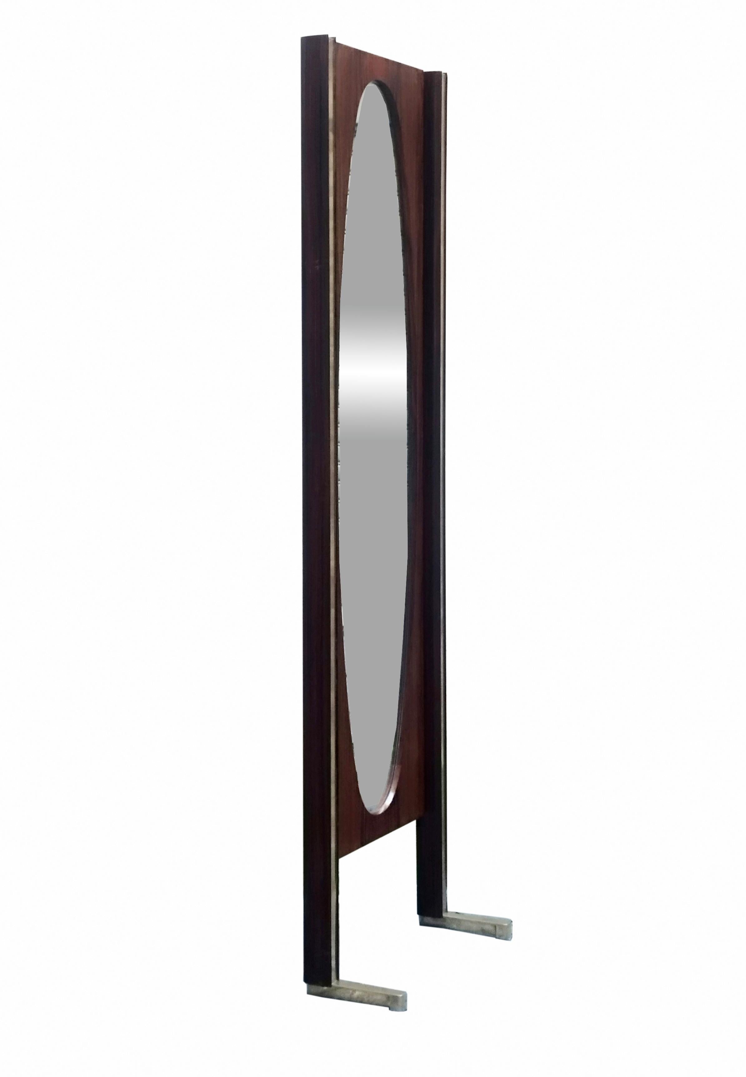 A rare Italian-made floor mirror produced in the 1960s, with a wooden frame and brass profiles resting on heavy brass feet. An oval mirror is mounted inside.
