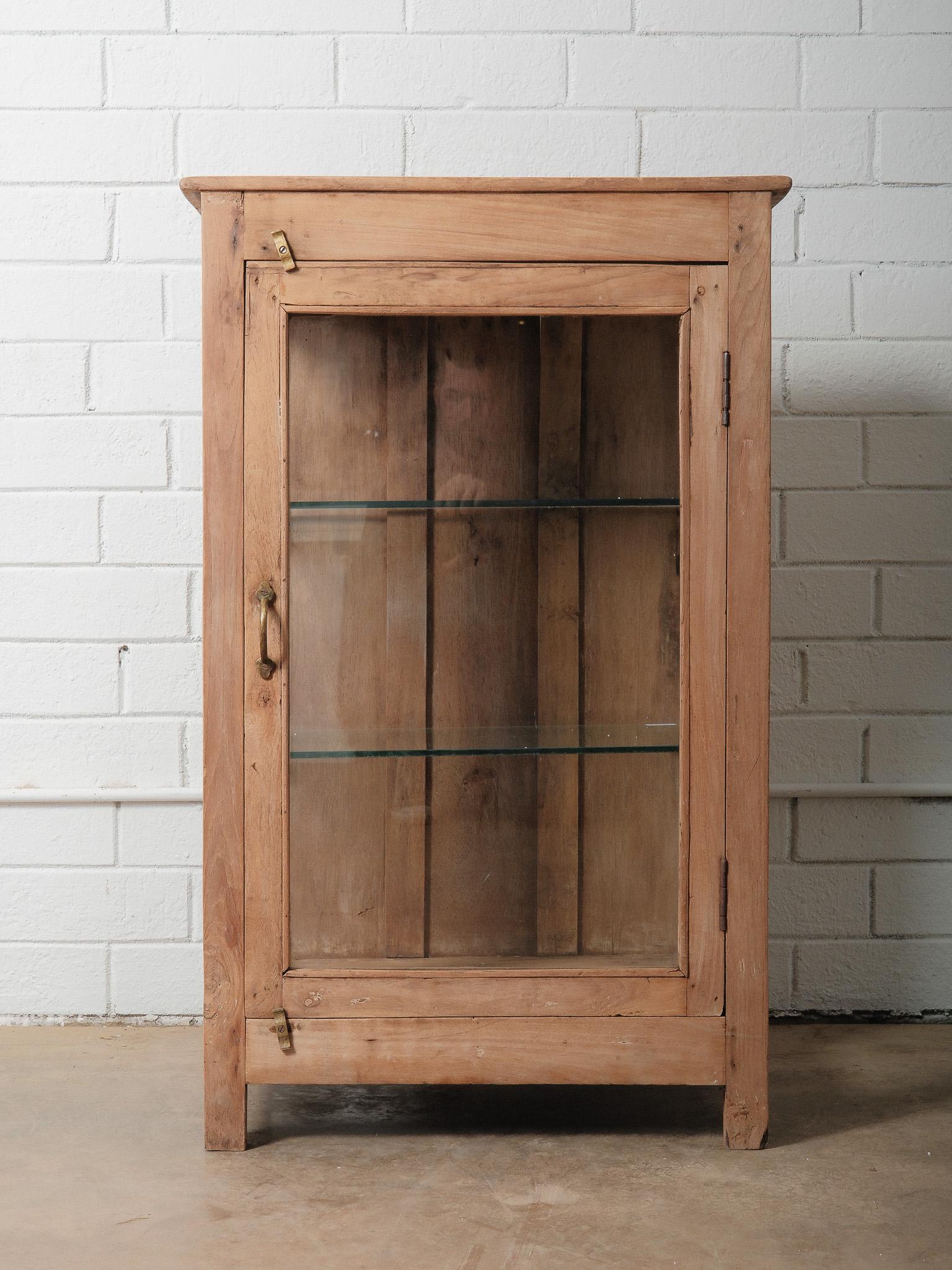 Un'affascinante vetrina vintage in legno e vetro con due lati in vetro, un'anta frontale in vetro e un unico ripiano interno in vetro. Questo pezzo presenta una finitura sverniciata e naturale che mette in evidenza le venature grezze, i nodi e i