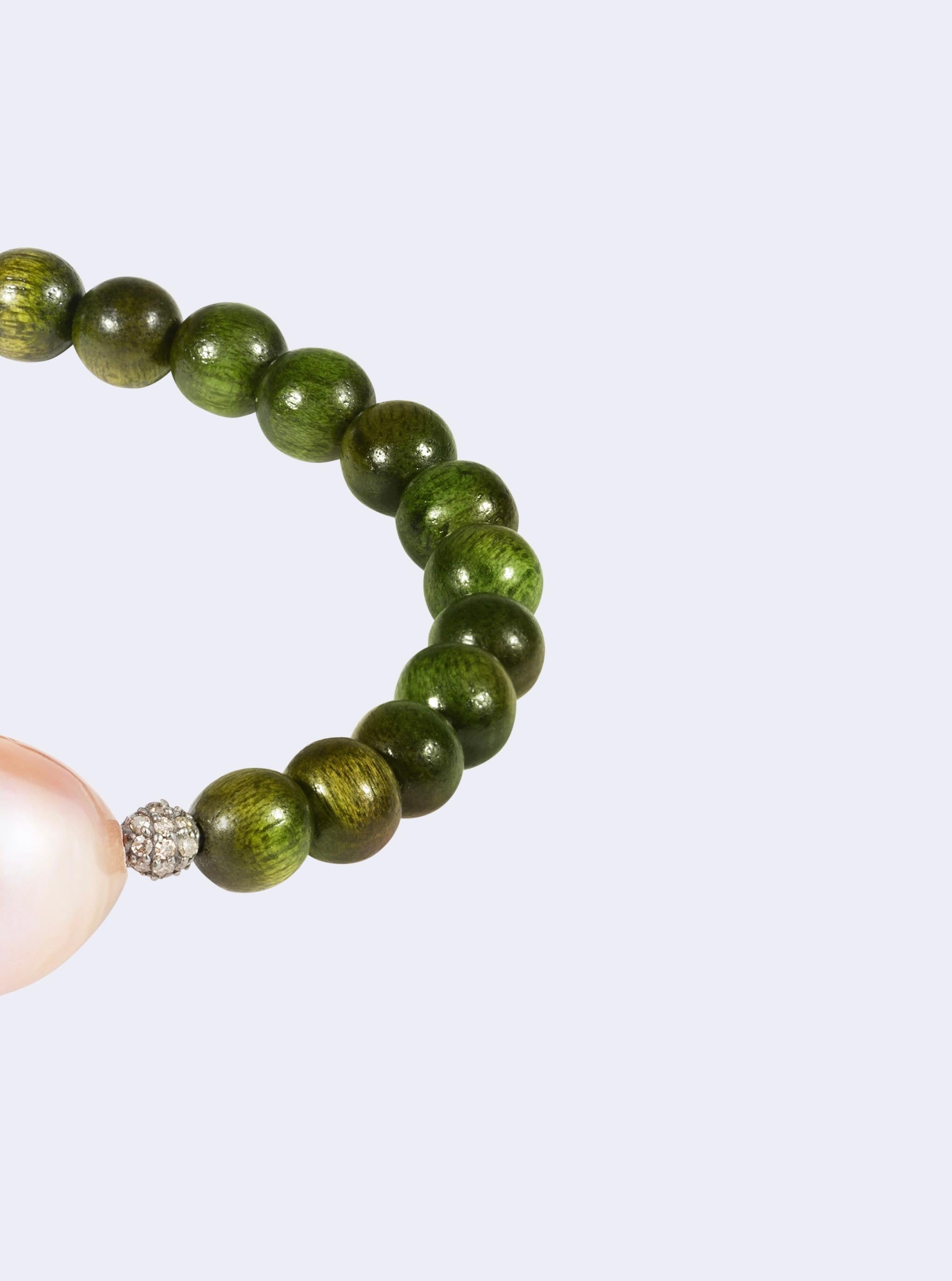 Discover elegance and charm with our exquisite green wooden beads bracelet, adorned with a large, lustrous baroque freshwater pearl in a captivating pink hue. Enhancing its allure are two meticulously crafted diamond-encrusted silver beads, each