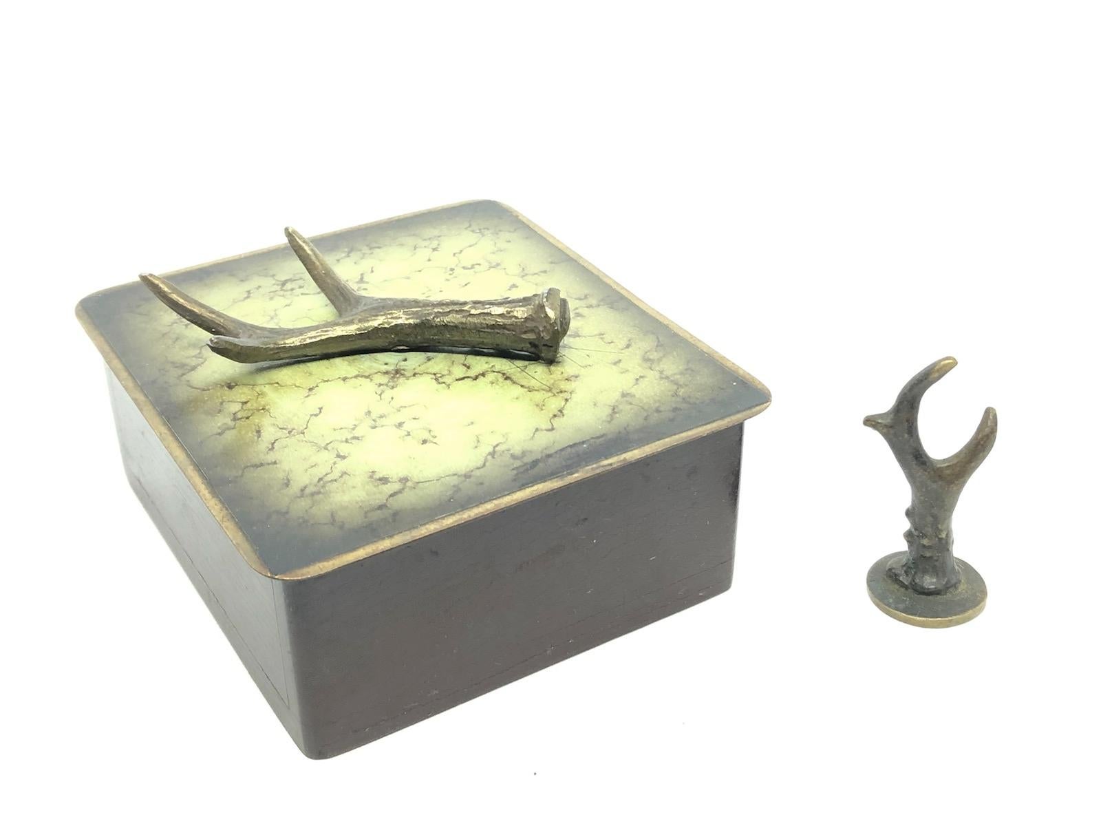 A beautiful wooden cigar or cigarette box with a bronze lid, has a bronze antler on the top as a handle. Also a little figure to use in your ashtray to kill the embers of your cigar or cigarette, it is in the form of a deer antler made also from