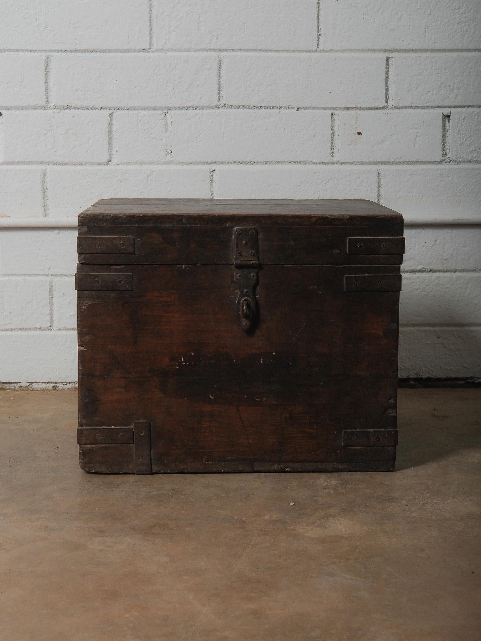 A wooden box with a hinged lid and iron fittings, constructed with simple joined panels and reinforced at the edges. The surface shows a deep, worn finish that has softened over time, with variations in tone and areas of natural abrasion. The lid