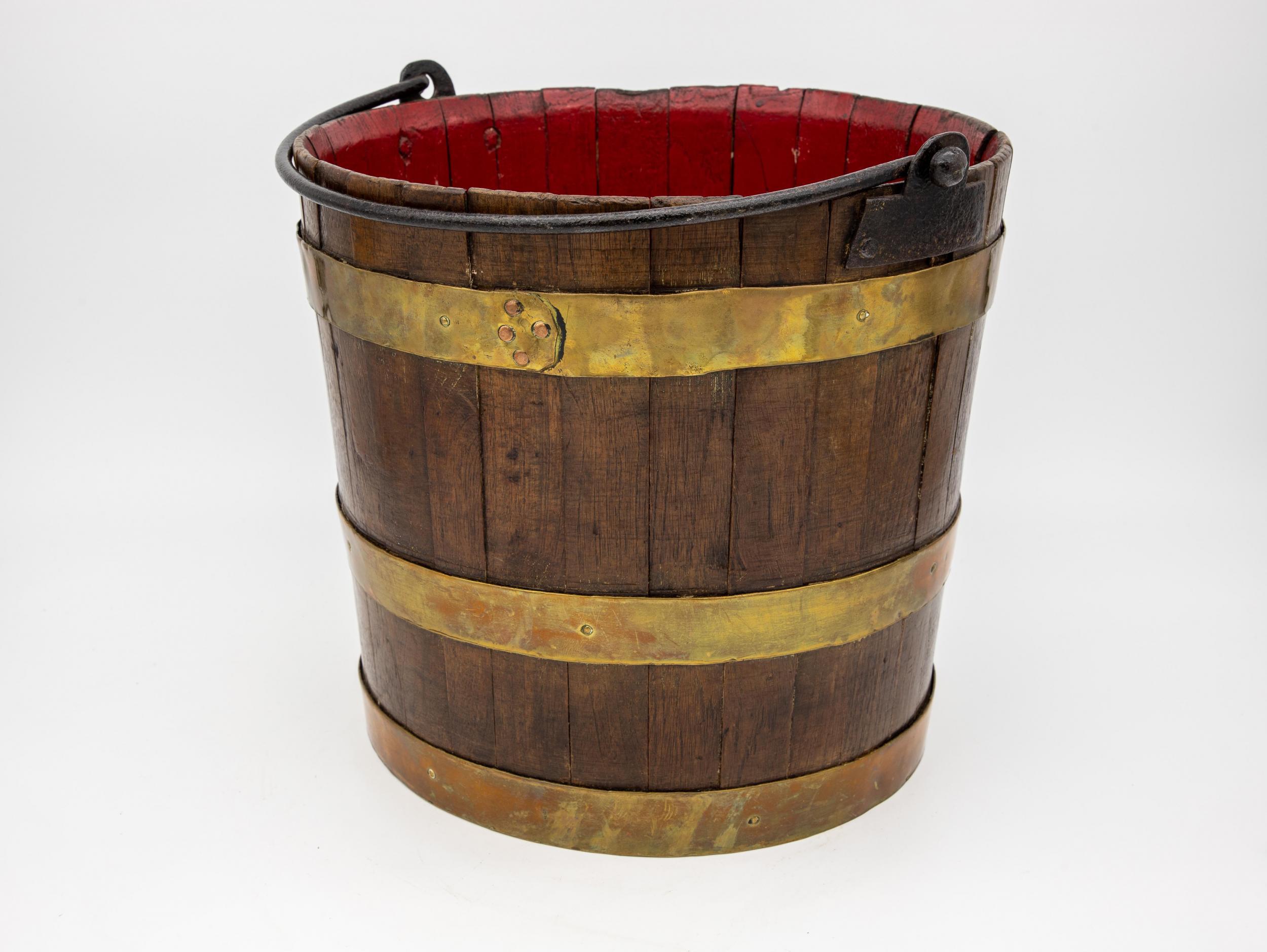 An antique coopered wood bucket. Brass fittings around the bucket with an iron handle. Interior of the bucket was later painted in a bright red. Ca.1870.