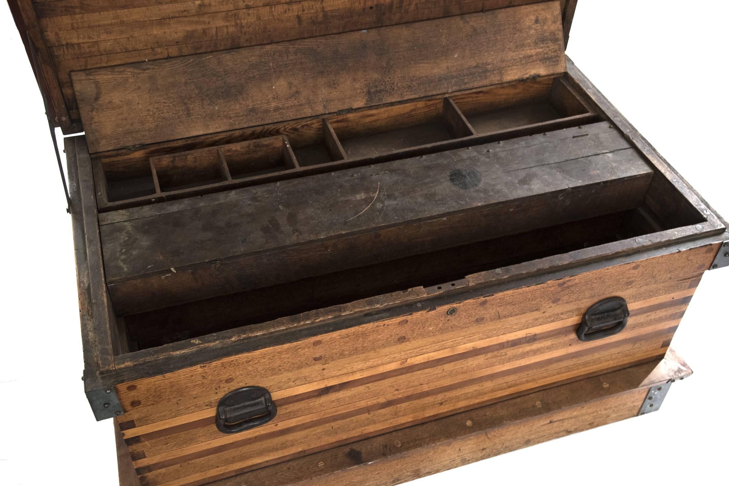 An early 20th century cabinet maker's tool chest constructed of alternating bands of different woods with half lap corners and some steel corner brackets for reinforcement, all sides mounted with iron handles and raised on a wider kick-board base.