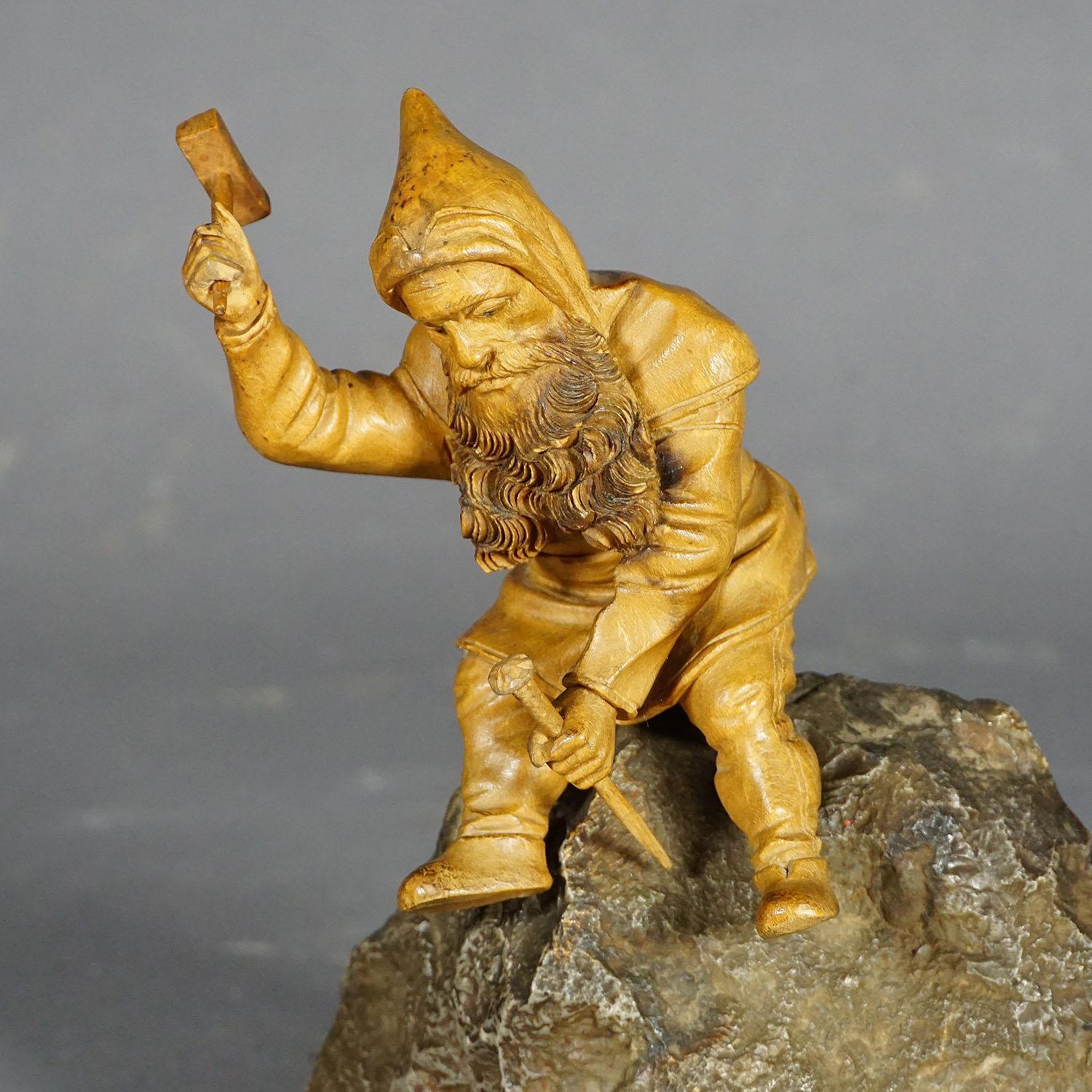 A wooden handcarved miner dwarf mounted on a small rock. The lindenwood design is manufactured in Switzerland, Brienz ca. 1900. The gnom has a hammer and chisel in his hands and works on the stone on which he sits. In mythology, dwarvers were