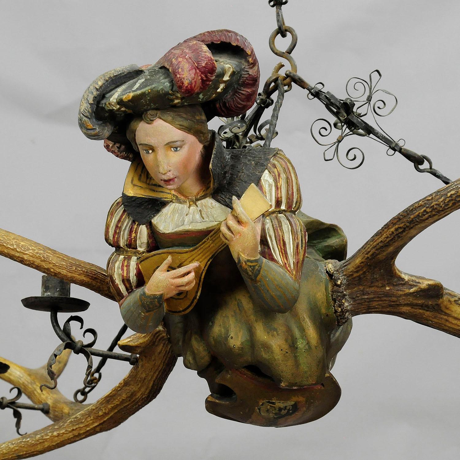 A small wooden carved antique Lüsterweibchen chandelier with a medieval lady playing the lute, original deer antlers, four hand-forged iron spouts for candles and a hand-forged suspension. Executed, circa 1890.

Measures: Length 33.46