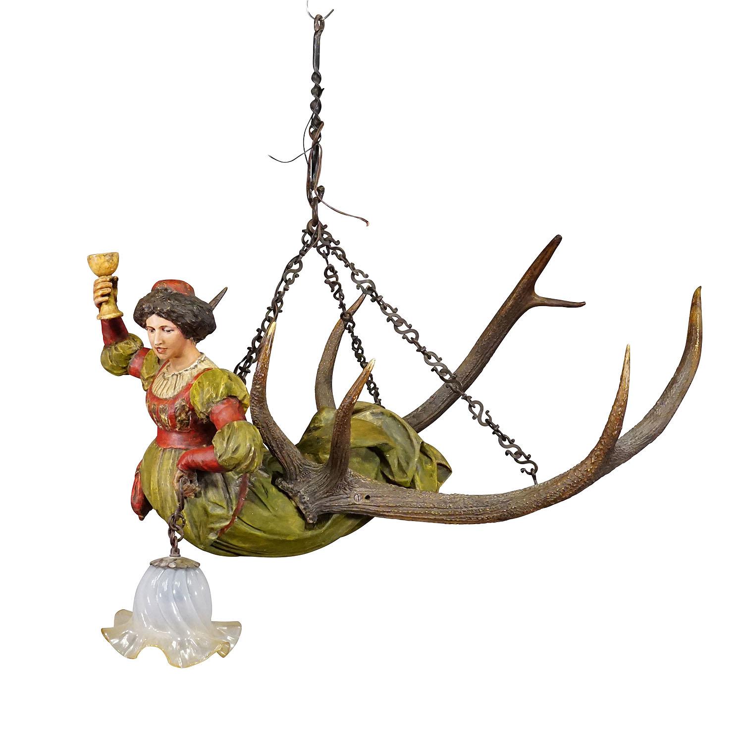Wooden Carved Lusterweibchen of a Medieval Noble Lady ca. 1900
Item e7362
An antique lusterweibchen with a hand carved and stained statue of a medieval lady with wine glass. Mounted on a pair of large deer trophys with hand forged iron suspension.