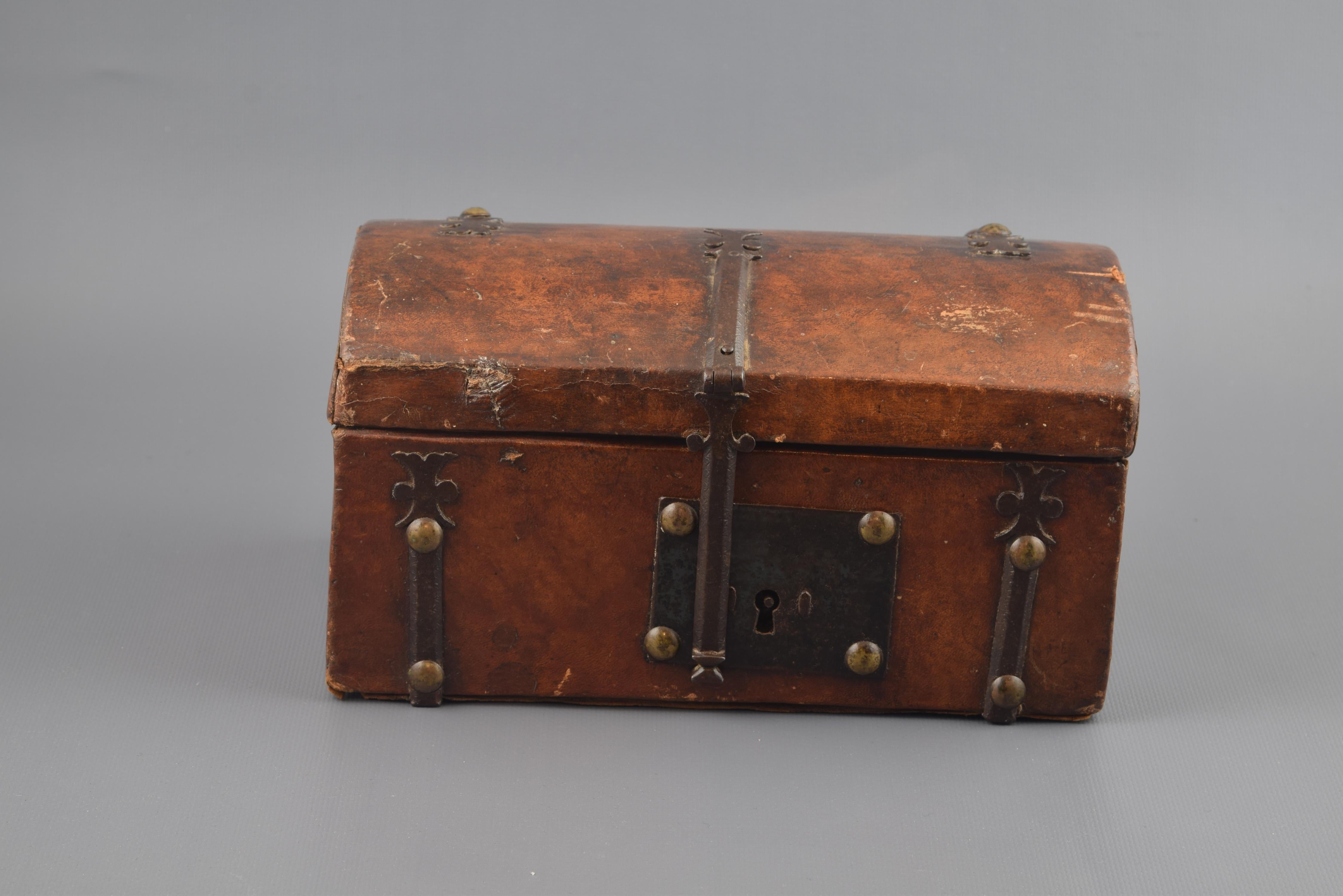 Rectangular casket with curved lid which is joined by hinges, made of carved wood and decorated to the outside with a worked leather cover (which also protects the interior) on which metal fasteners and fittings and a lock with rectangular shield.