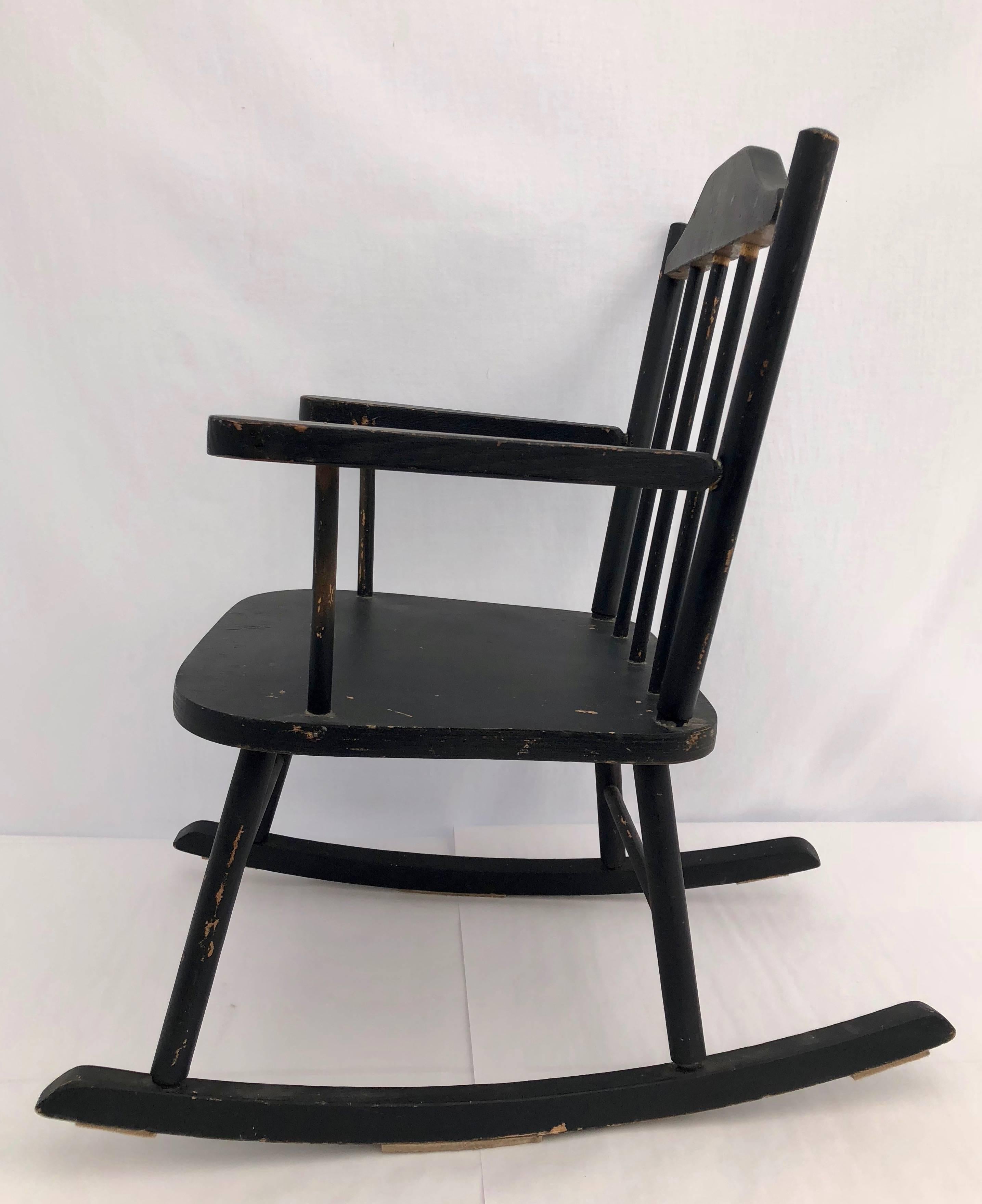 This is a lovely wooden child's rocking chair with a spindle back. It has been painted black and is simply charming.