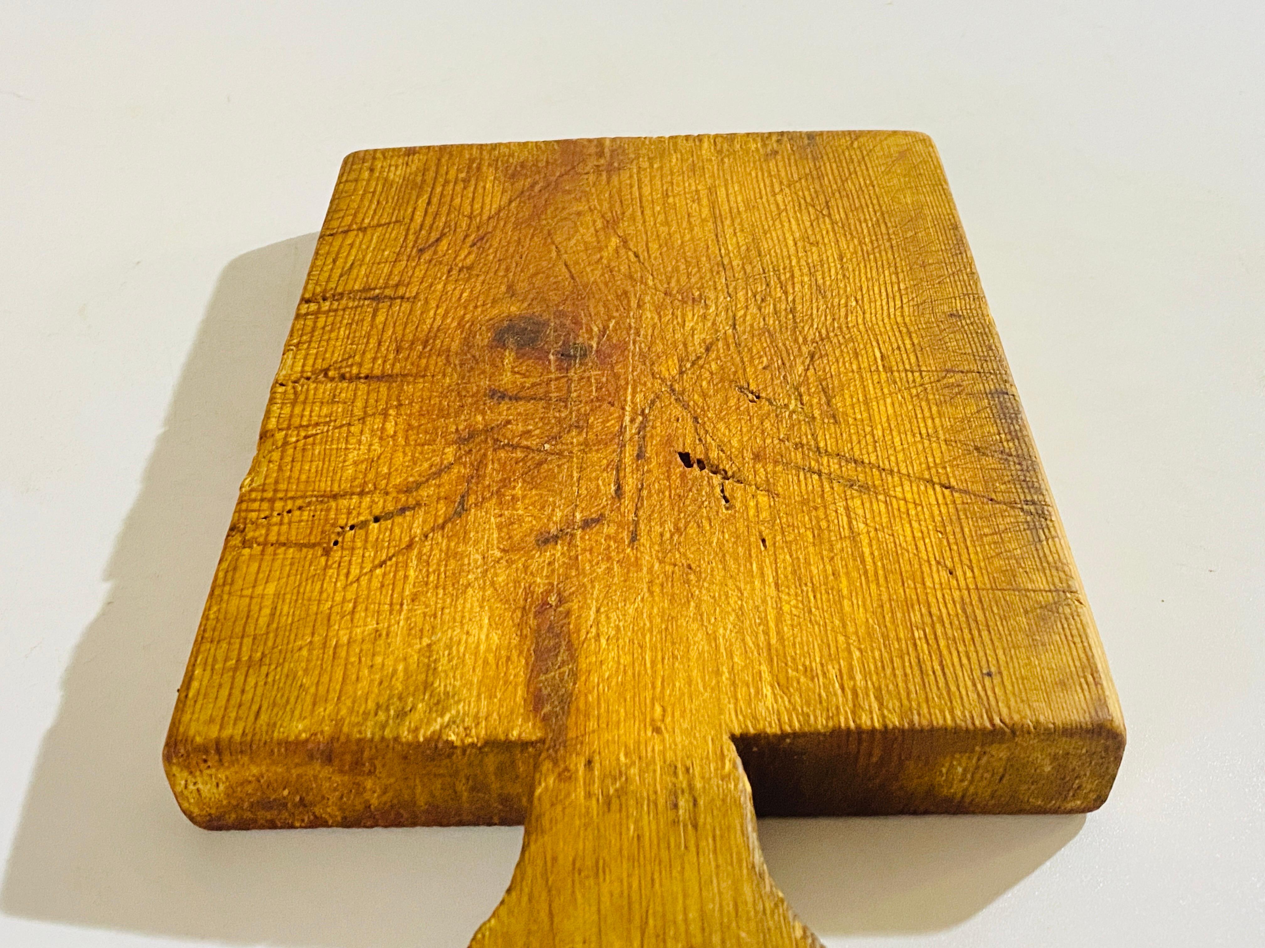 Planche à découper en bois, avec sa patine ancienne. Il s'agit d'un objet du XXe siècle français, dans le style French Provincial de couleur brune, et dans un état correspondant à son âge et à son utilisation.