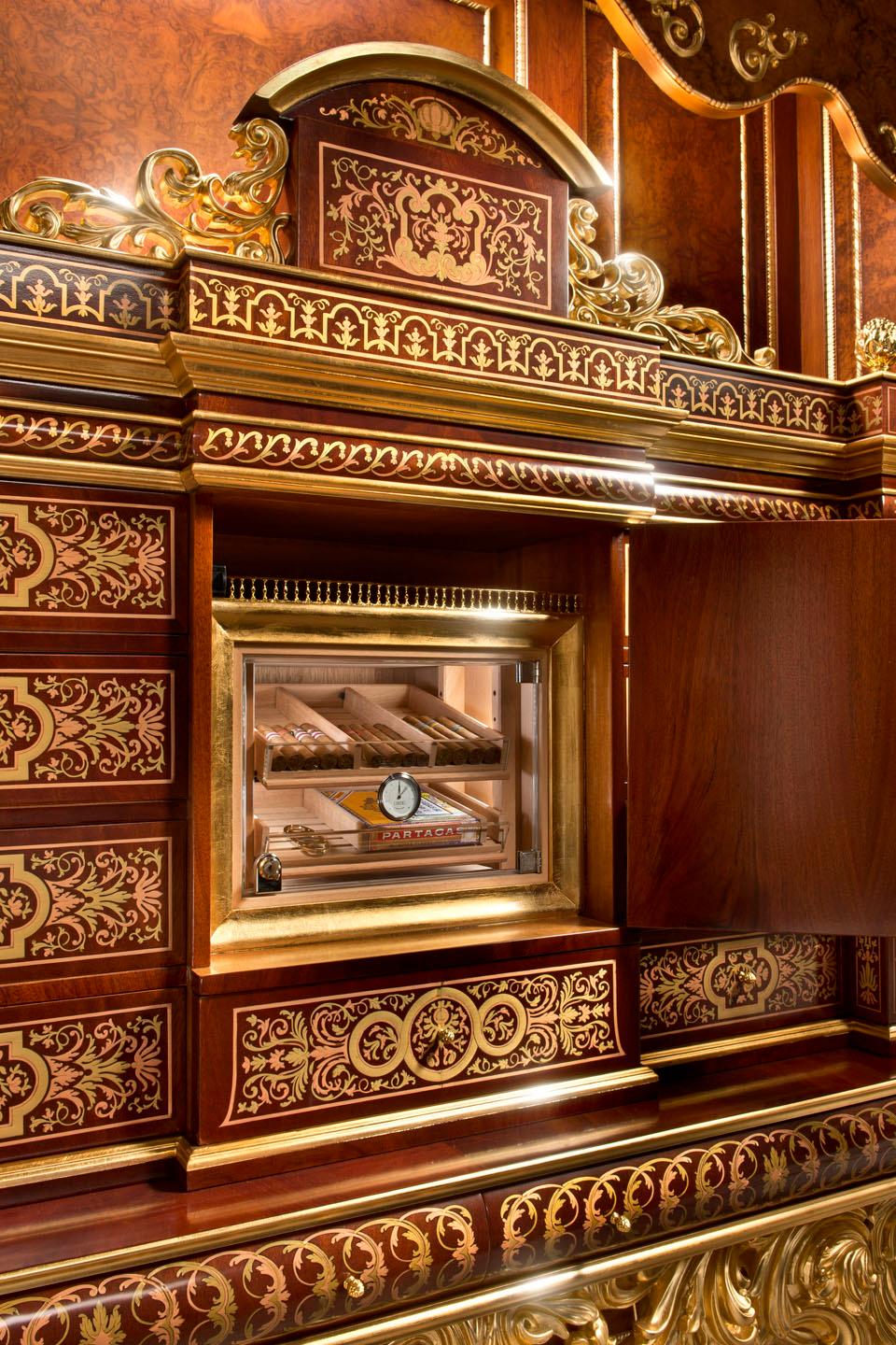 Massive Cigar cabinet with a solid wood high-end luxury structure decorated with breathtaking hand carved squiggles featuring shiny gold leaf applications. 
The upper wooden case presents a 9-drawers dark walnut inlay and hand-painted baroque