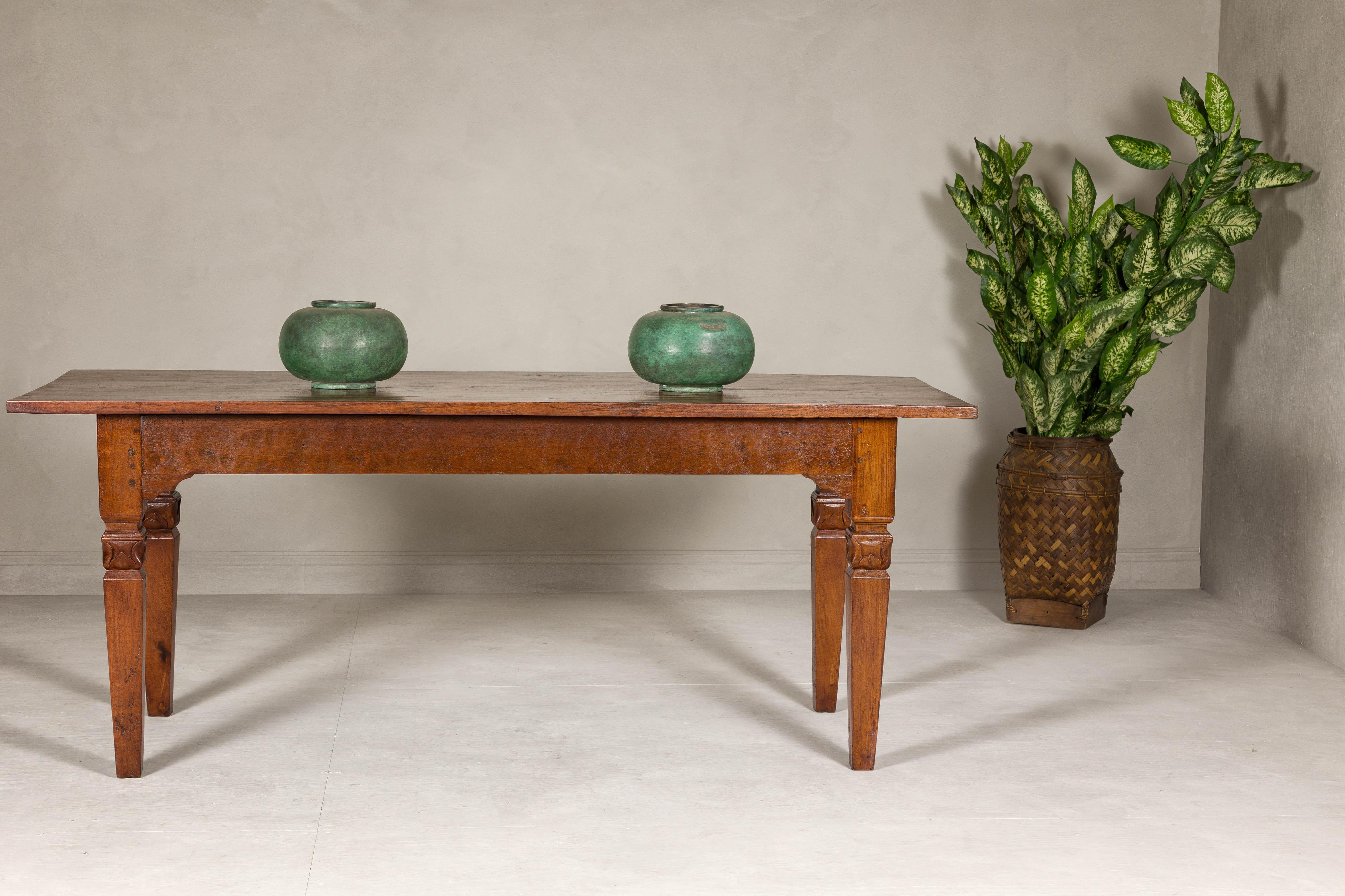 A wooden dining room table with carved lotiform capitals sitting atop the legs and custom finish with satin patina. This vintage wooden dining table, elegantly restored to its former glory, makes an exquisite addition to any dining room with its